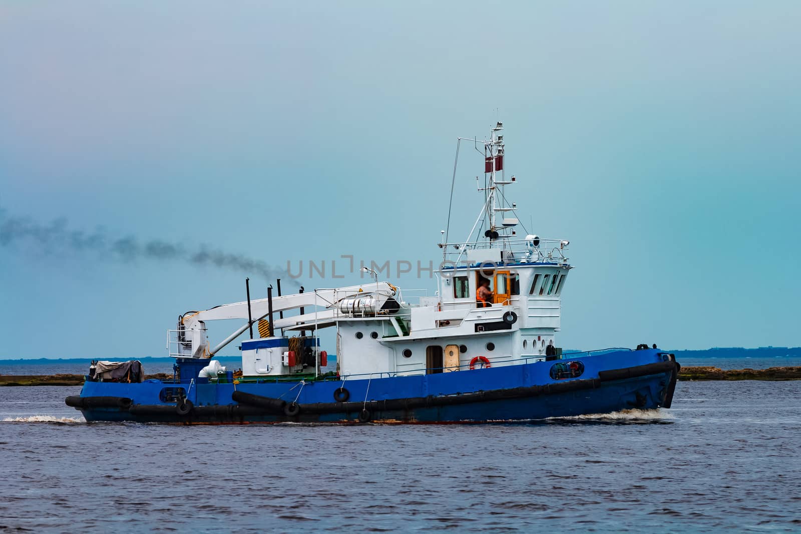 Blue tug ship moving to the cargo terminal. Industrial services