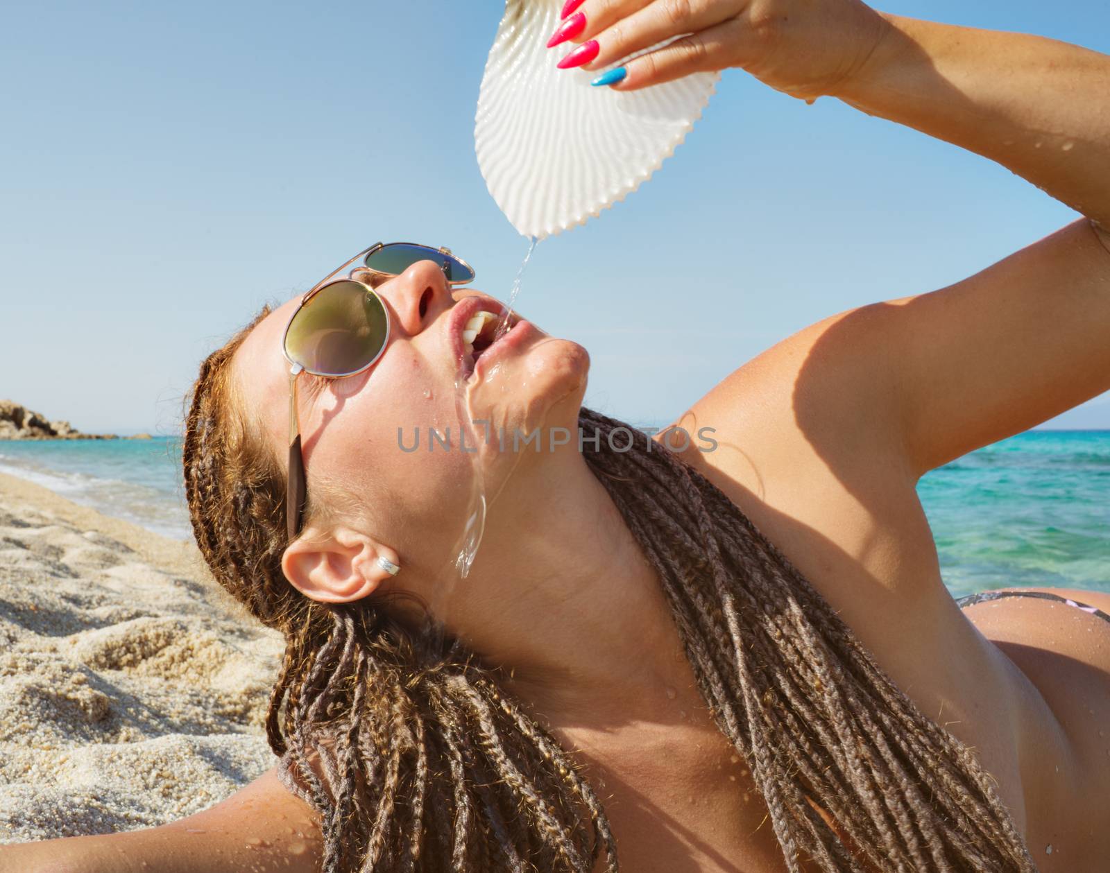 A beautiful girl is drinking water from a shell on a distant sea shore.