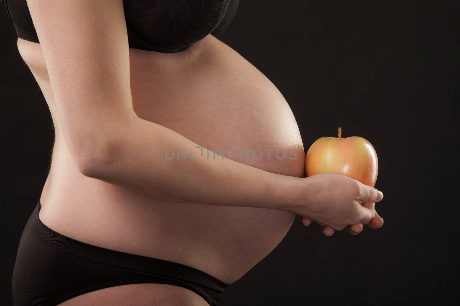 A pregnant female torso with apple in hands.