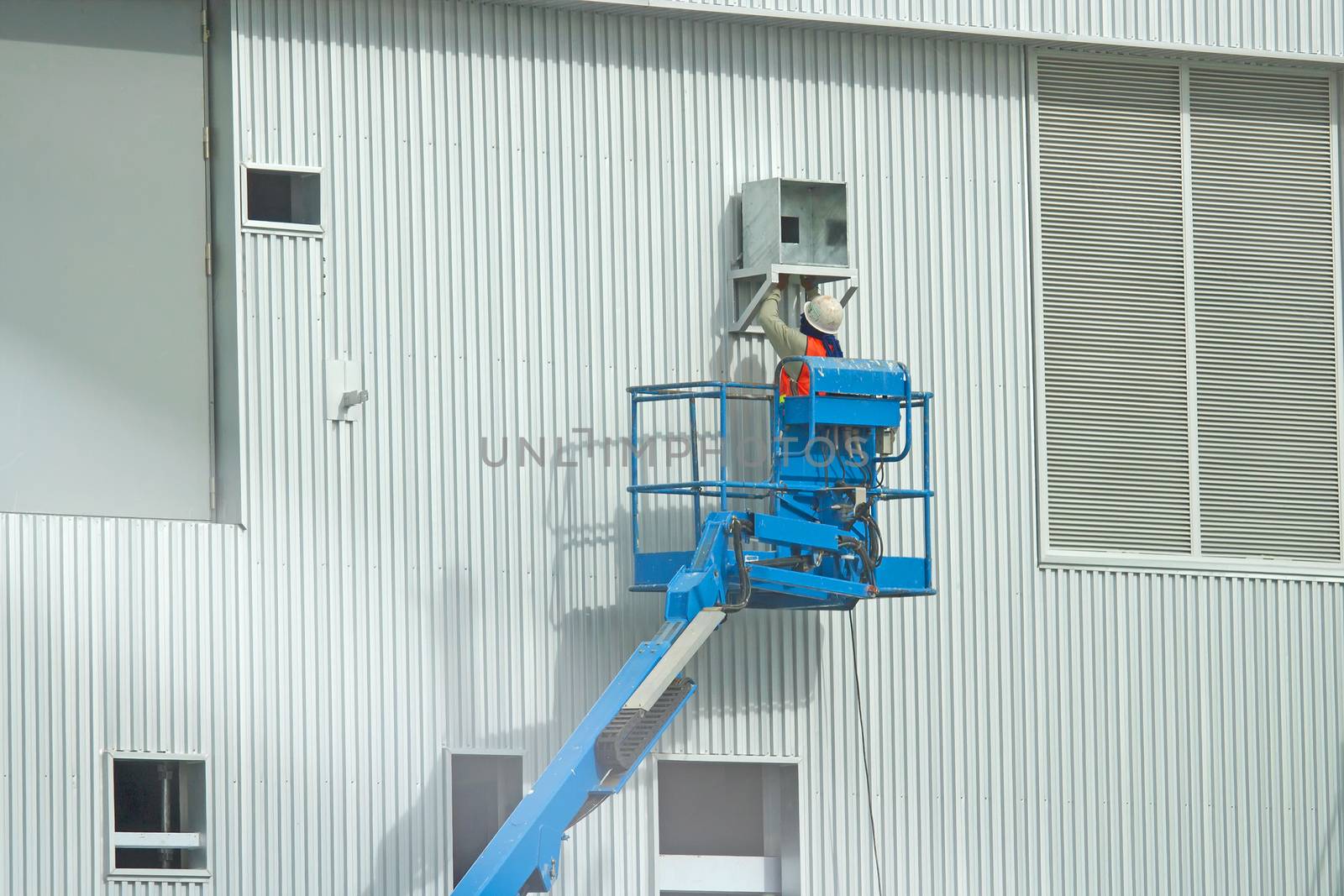 Workers in a baskets are installing sheet, building a factory.