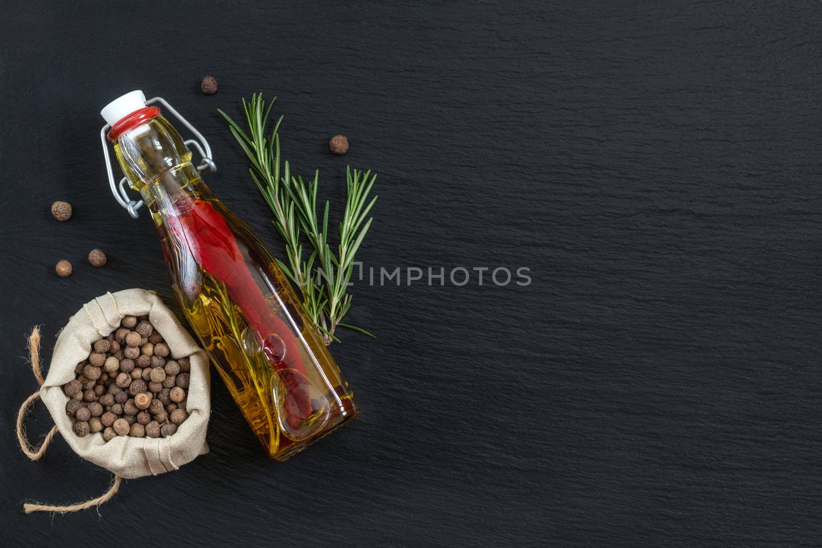 Rosemary bunch, olive oil with pepper and spices and fragrant pepper on black stone surface. Top view, copy space.