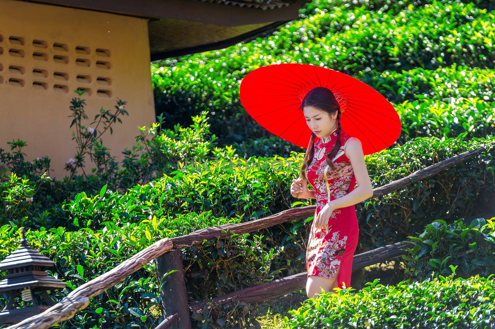 Asian woman wearing traditional Chinese dress and red umbrella in green tea field.