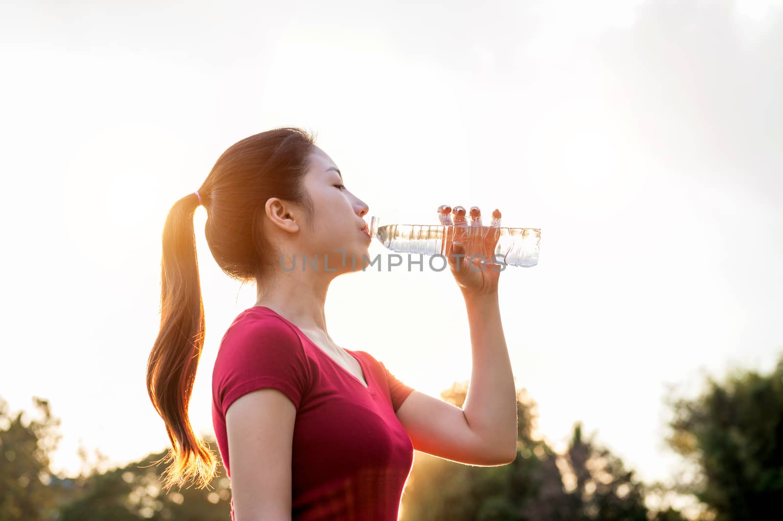 Sporty woman drinking water on sunlight. by gutarphotoghaphy