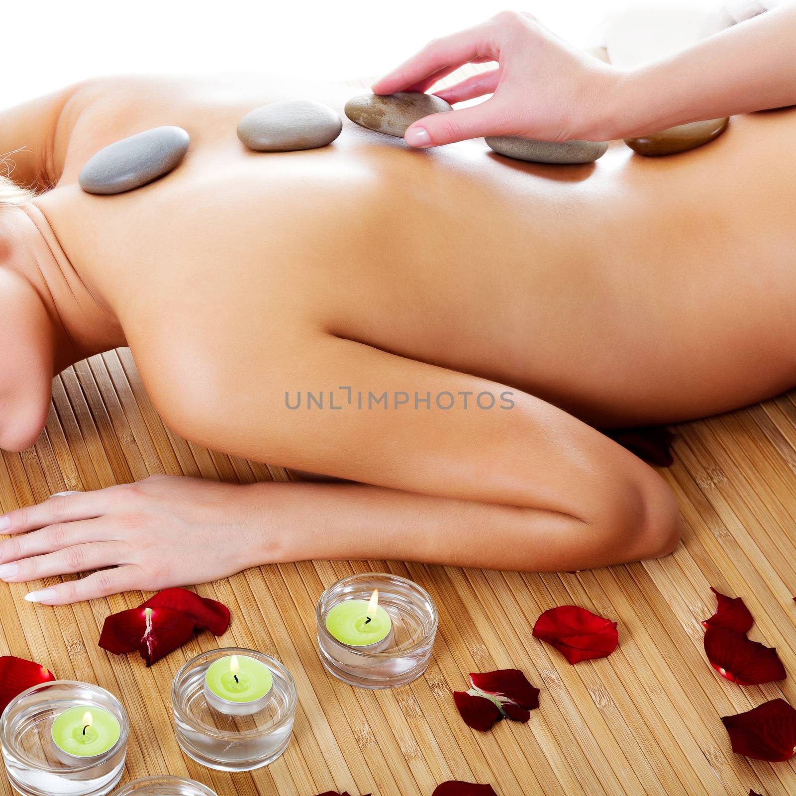 Woman at spa center, naked female back with hot stones on it