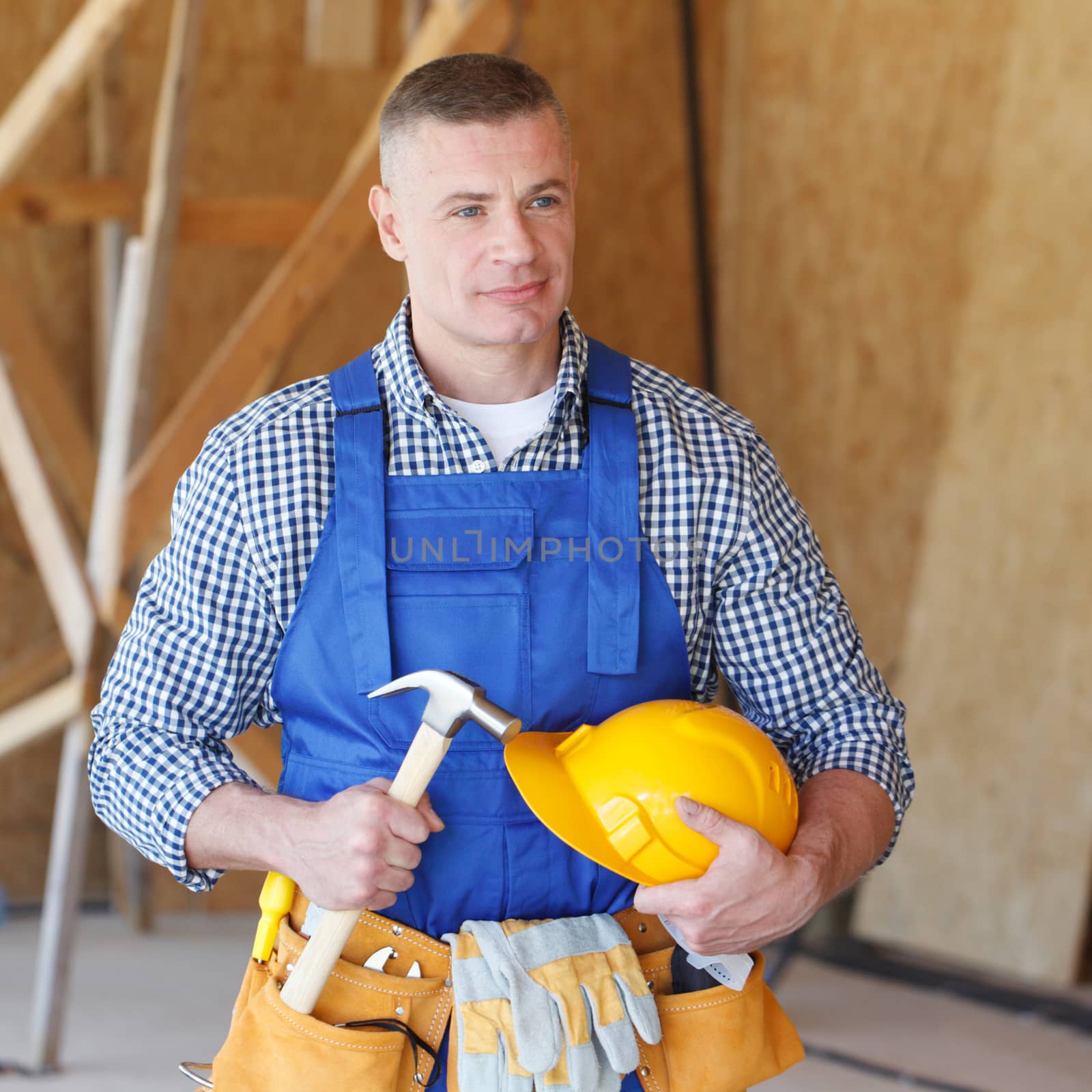 Portrait of construction worker at construction site holding hammer and hardhat