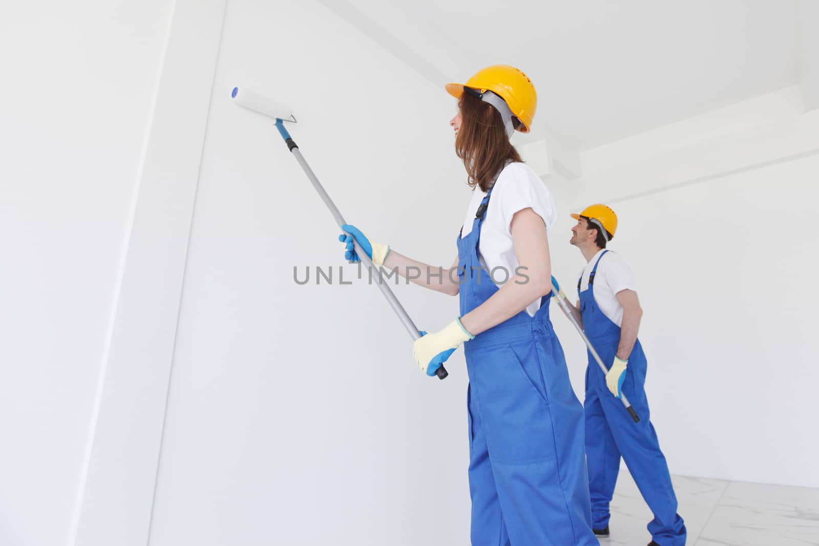 Two young workers in uniform painting the wall