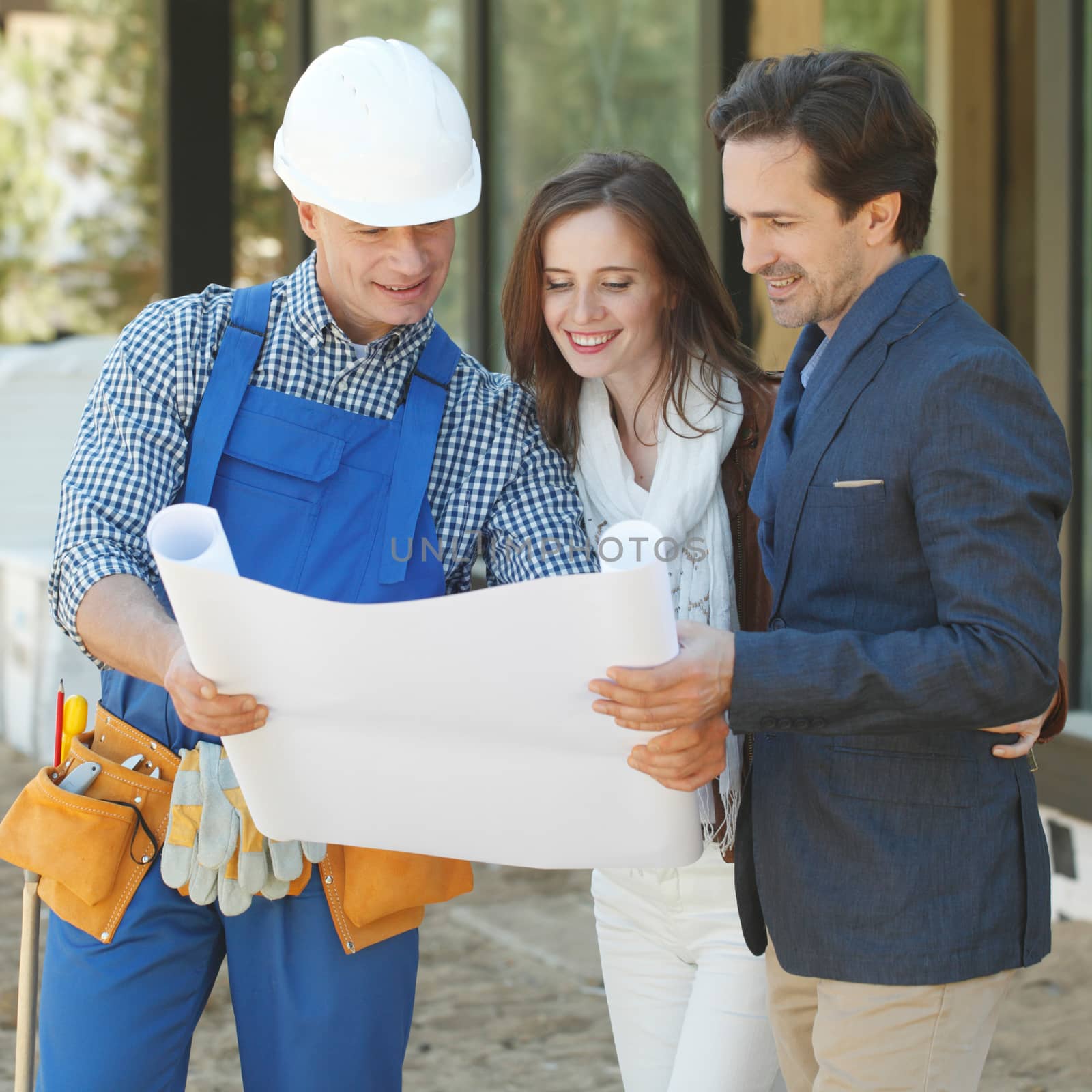 Worker shows house design plans to a young couple at construction site