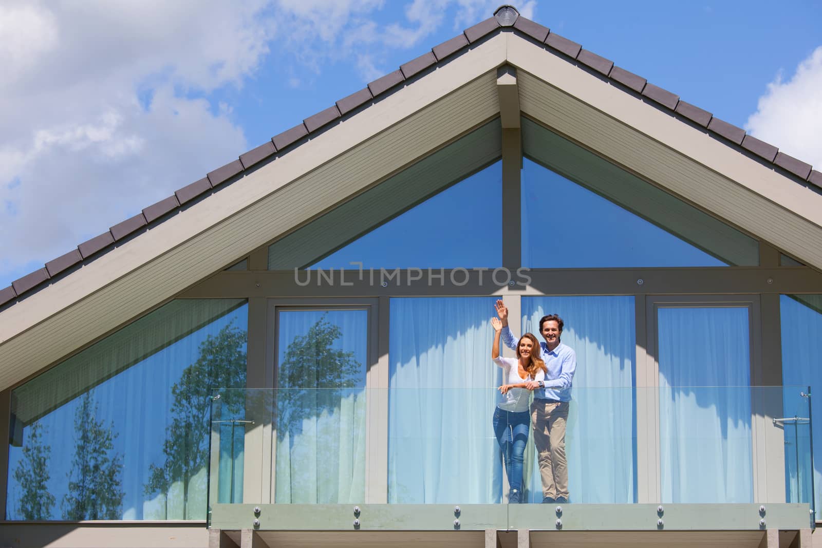 Happy couple standing on the balcony of their house and waving hands