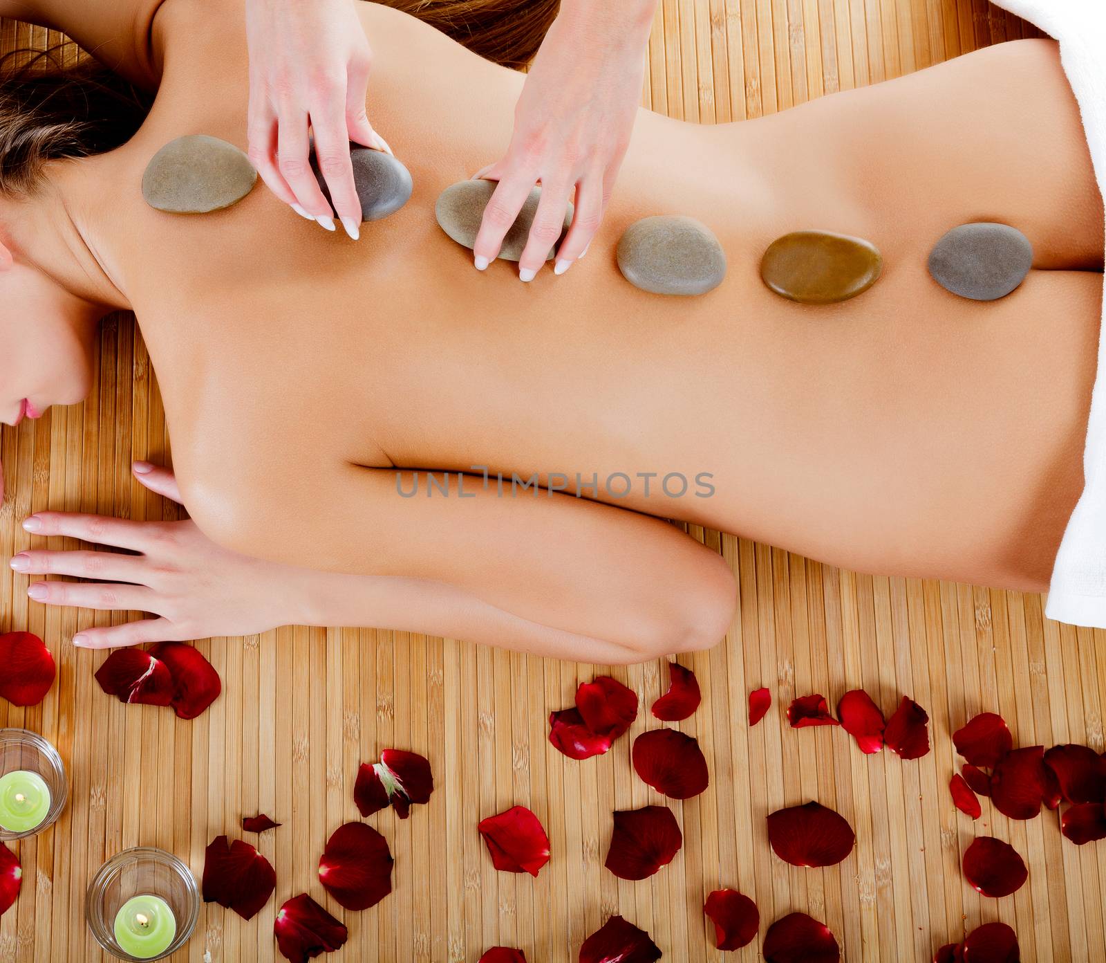 Woman at spa center, naked female back with hot stones on it by Nobilior