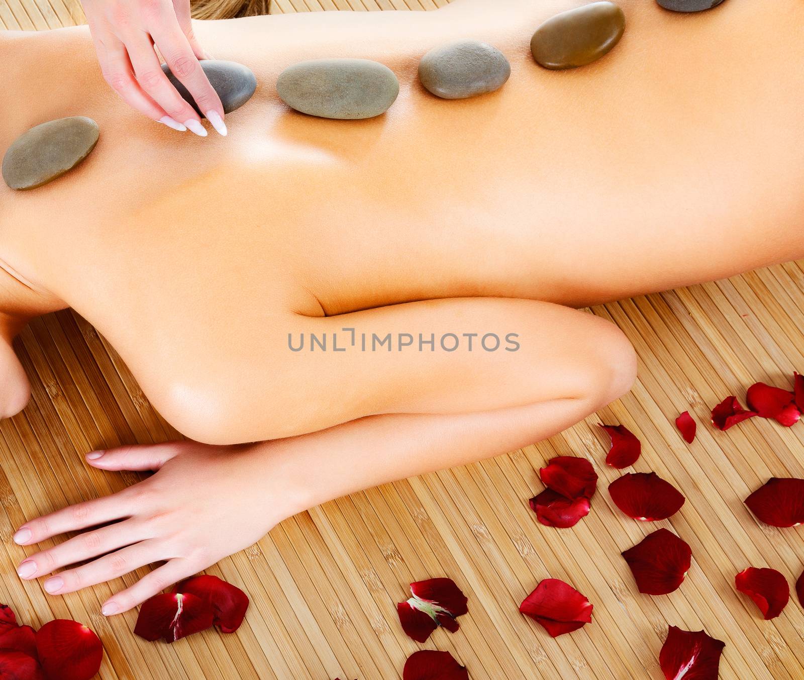 Woman at spa center, naked female back with hot stones on it by Nobilior