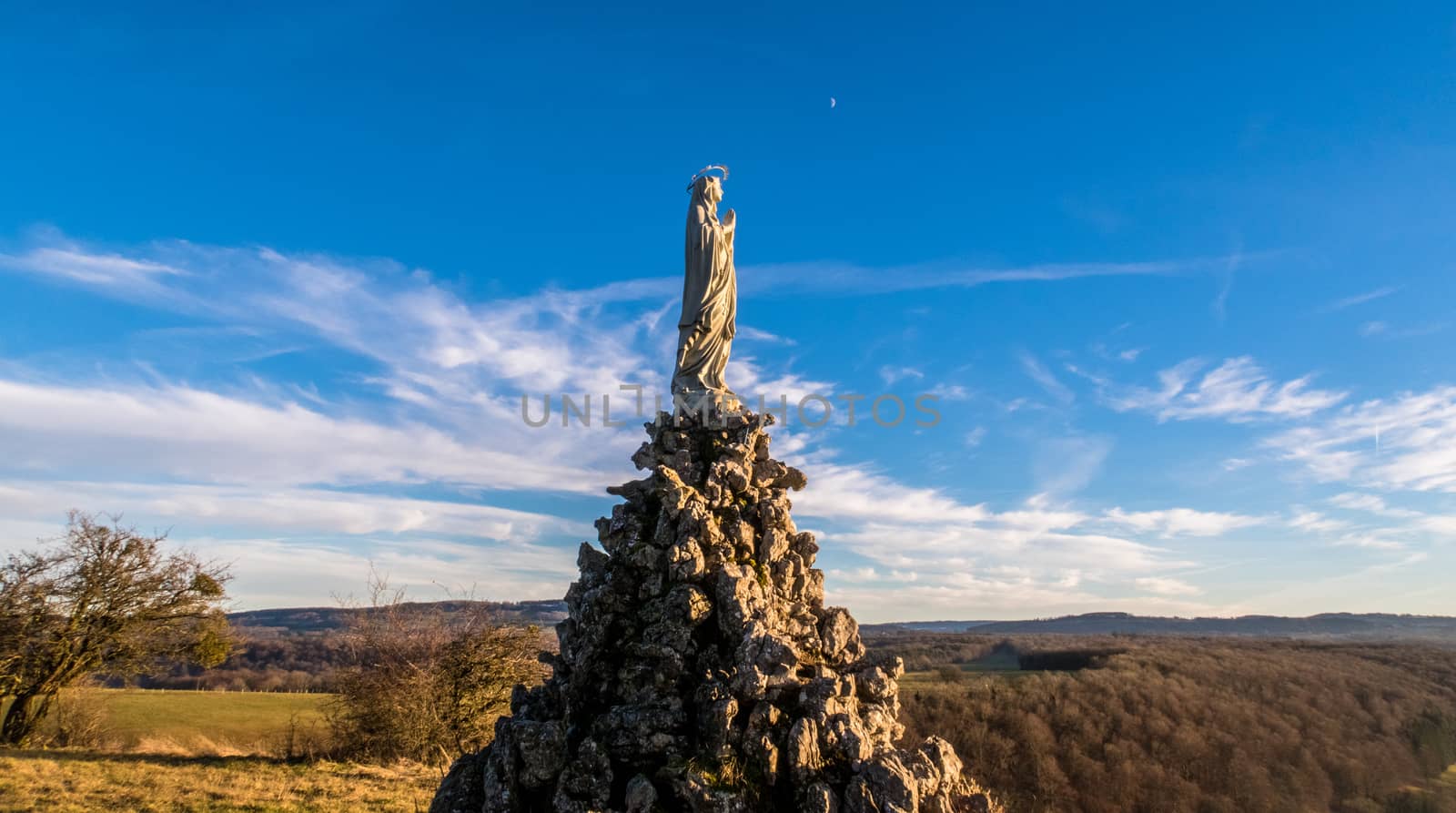 Wide angle shot from low angle of view of a Virgin Mary statue with moon and clouds on background.