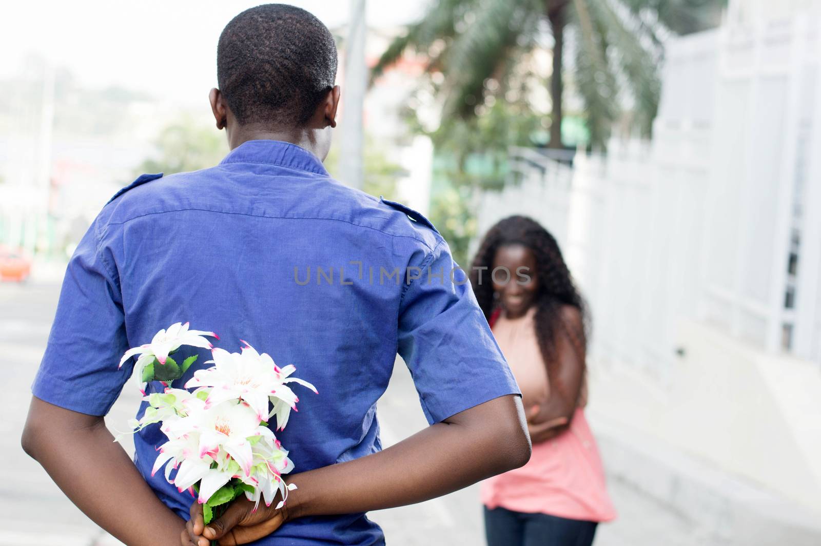 young man hides a flower in his back and give it to the young woman in surprise.