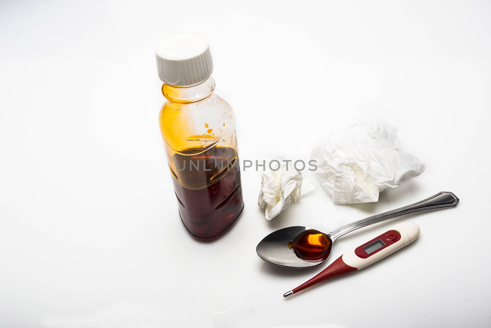 Cough sirop in a spoon and old tissue on a white background