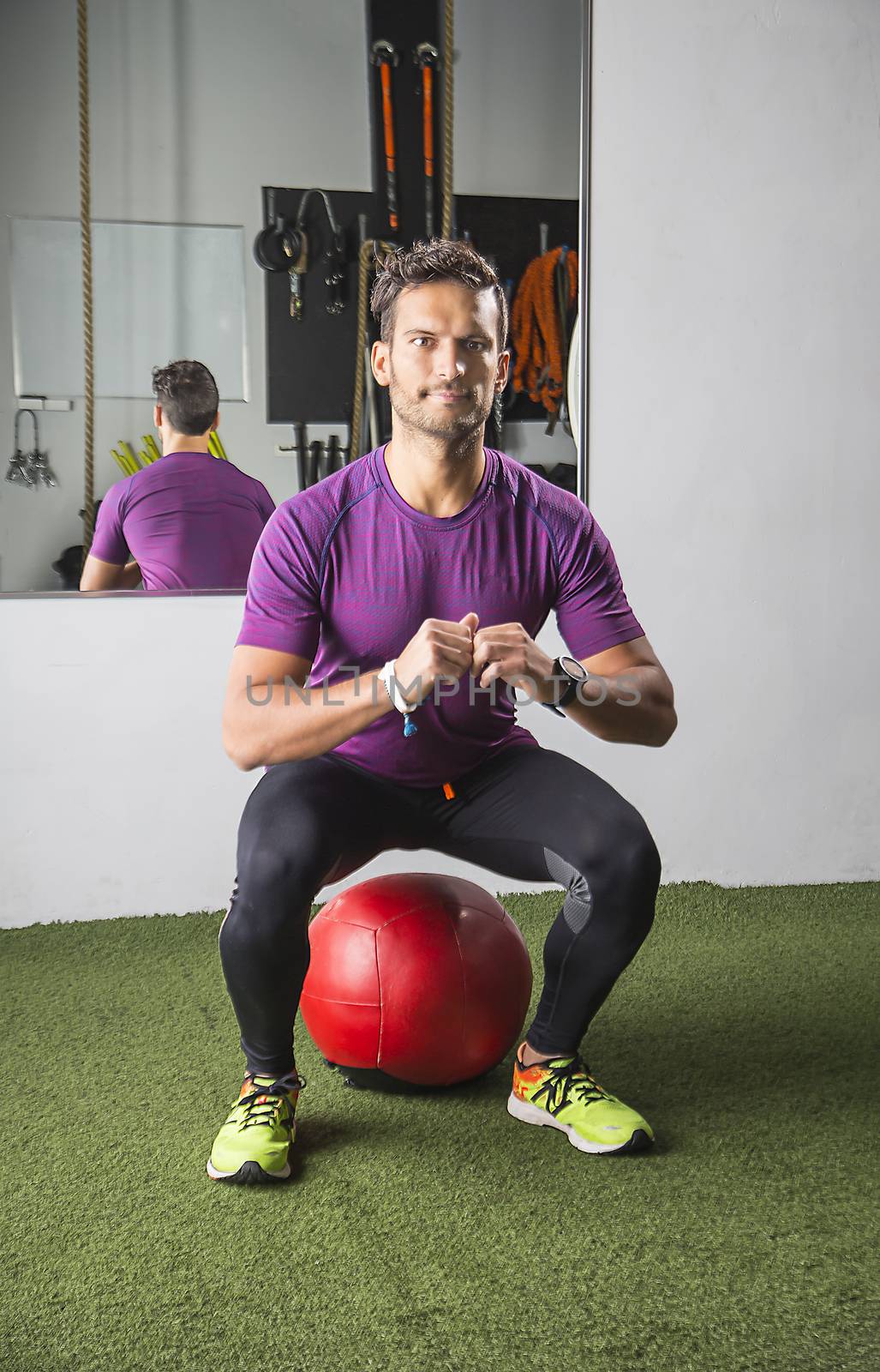 Man in his thirties doing a squat over a red medicine ball