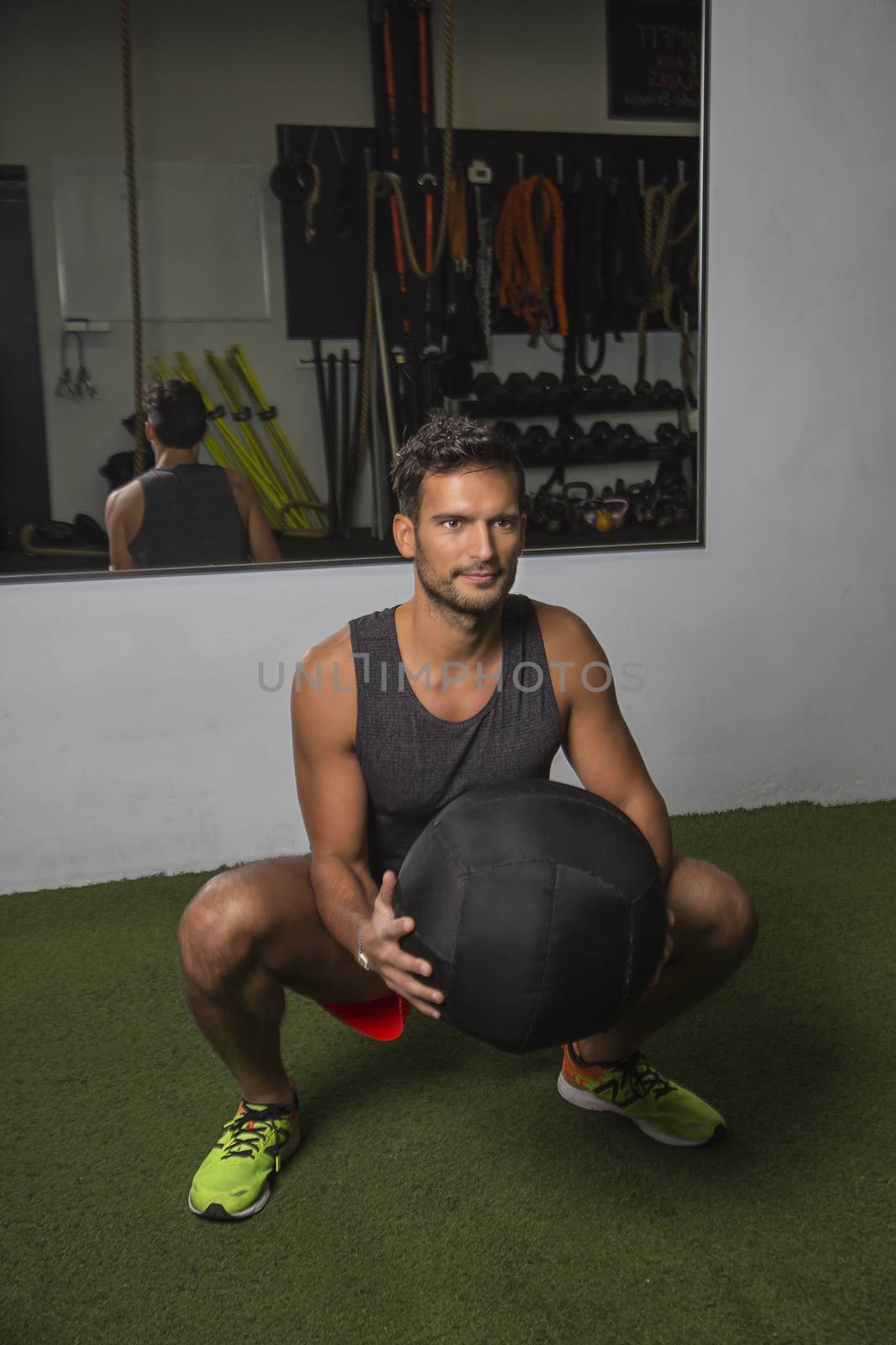 young man holding a large medicine ball, doing a squat