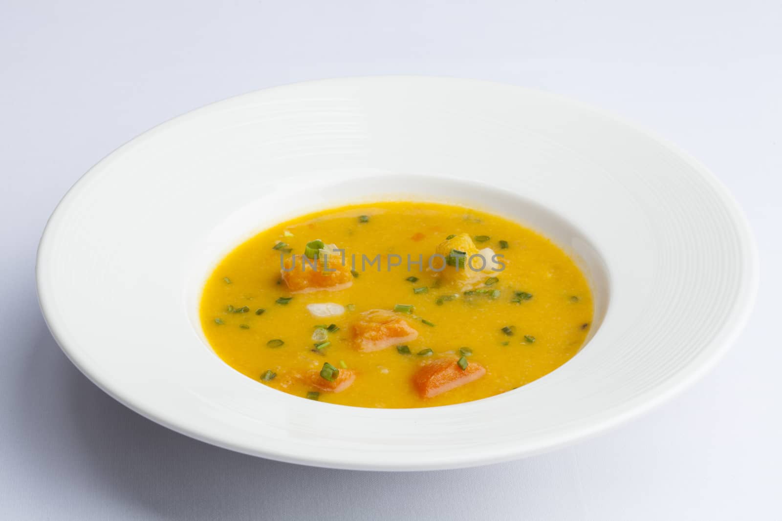 Pumpkin soup with cream and pumpkin seeds on white background.