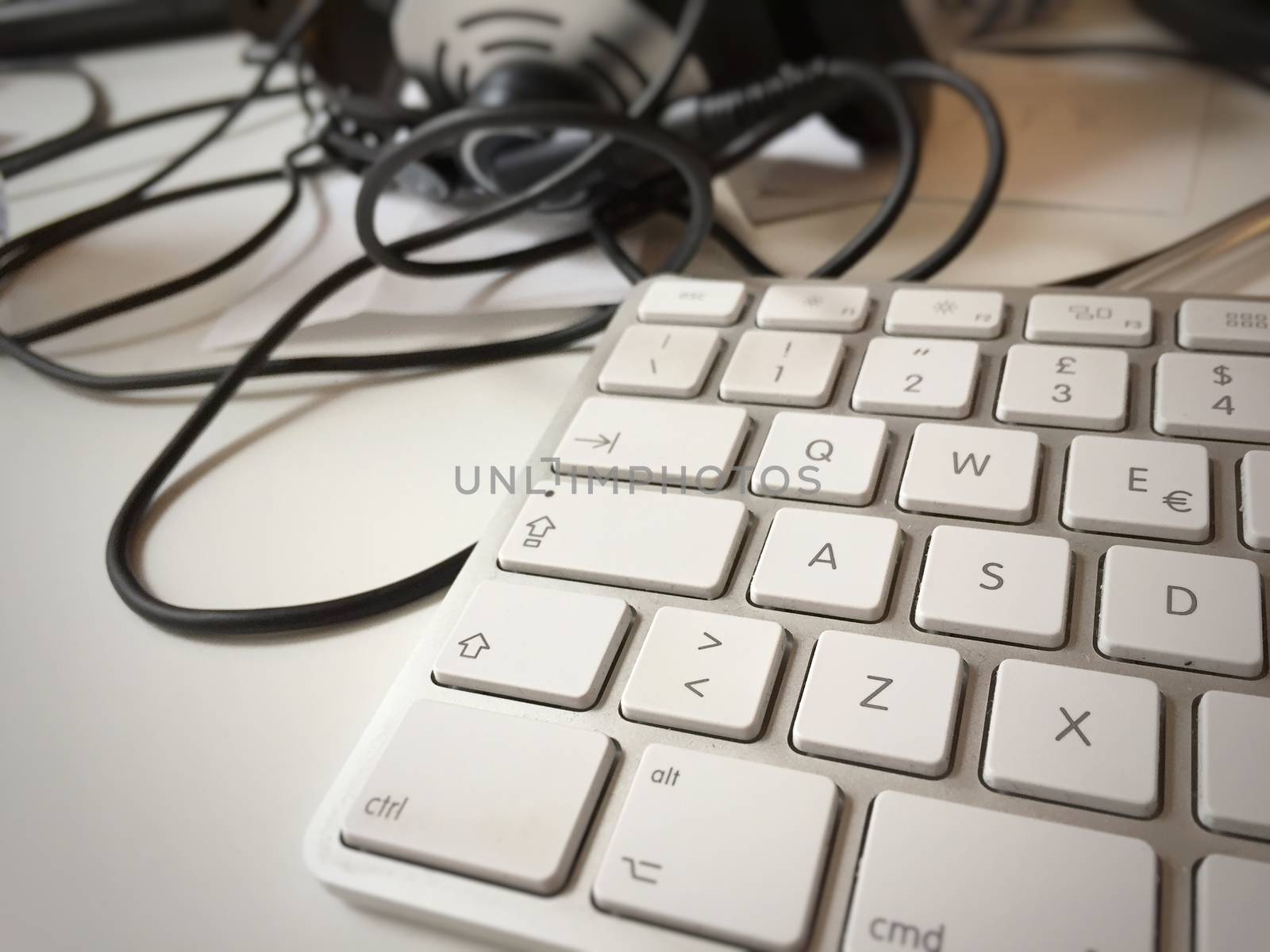 close-up view of a modern white PC keyboard with headphones on the blurred background