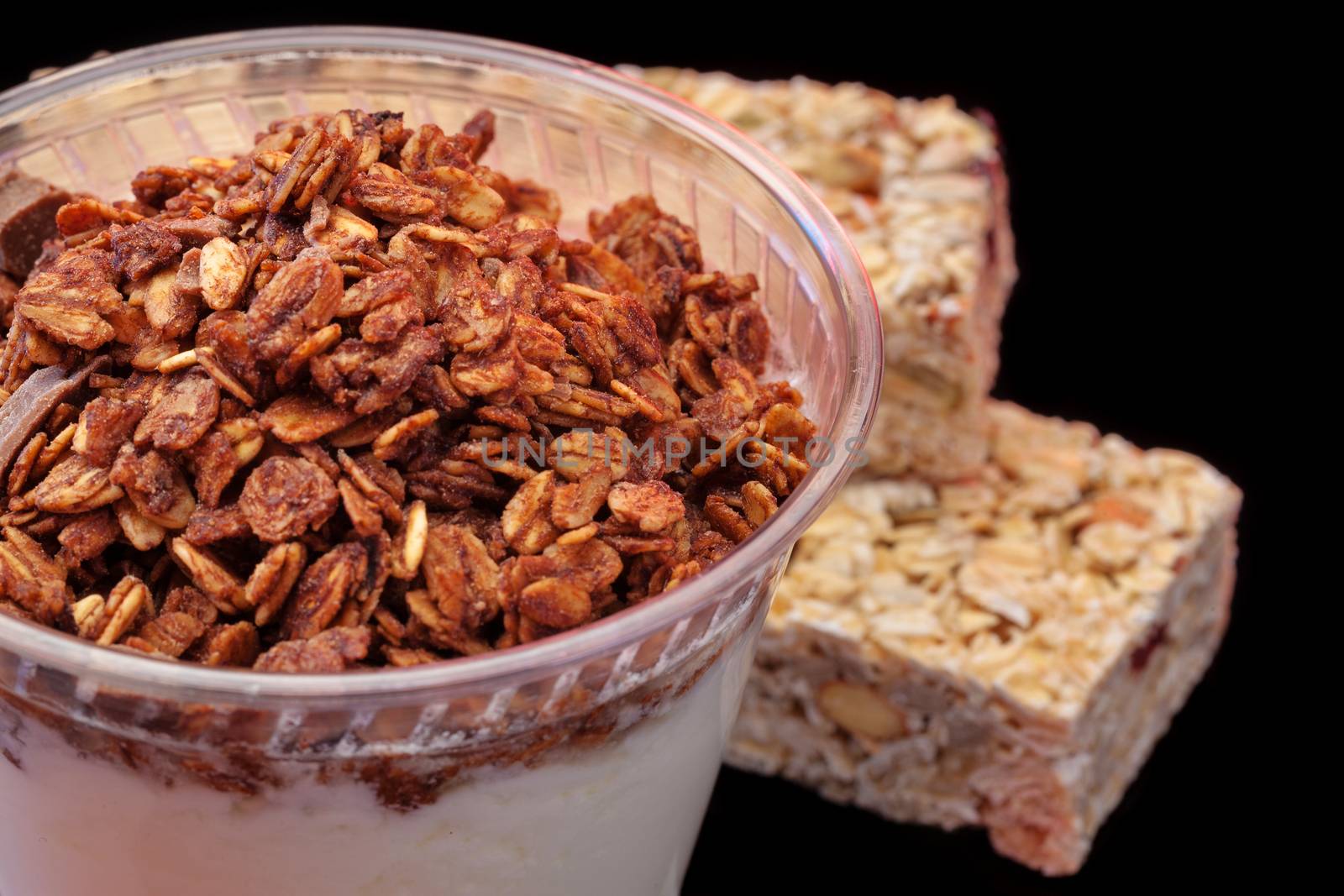 Yogurt with chocolade granola and granola bar with fruits and nuts on black background with copyspace