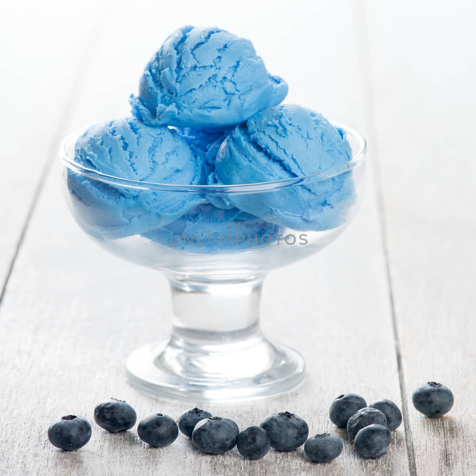 Blue ice cream in cup with blueberry fruits on wooden background.