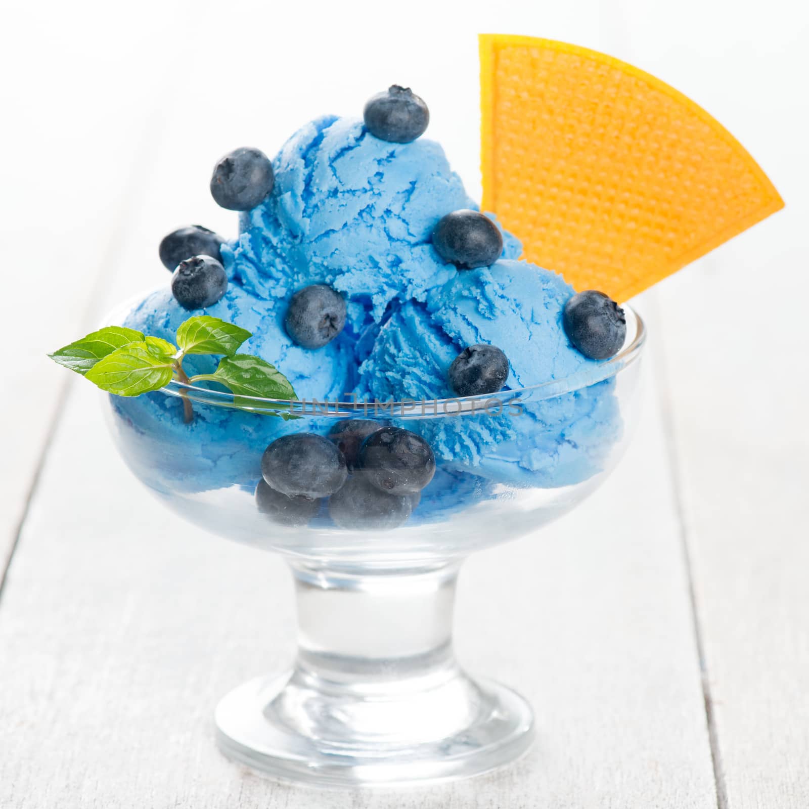Blue ice cream in cup with blueberry fruits on white wooden background.