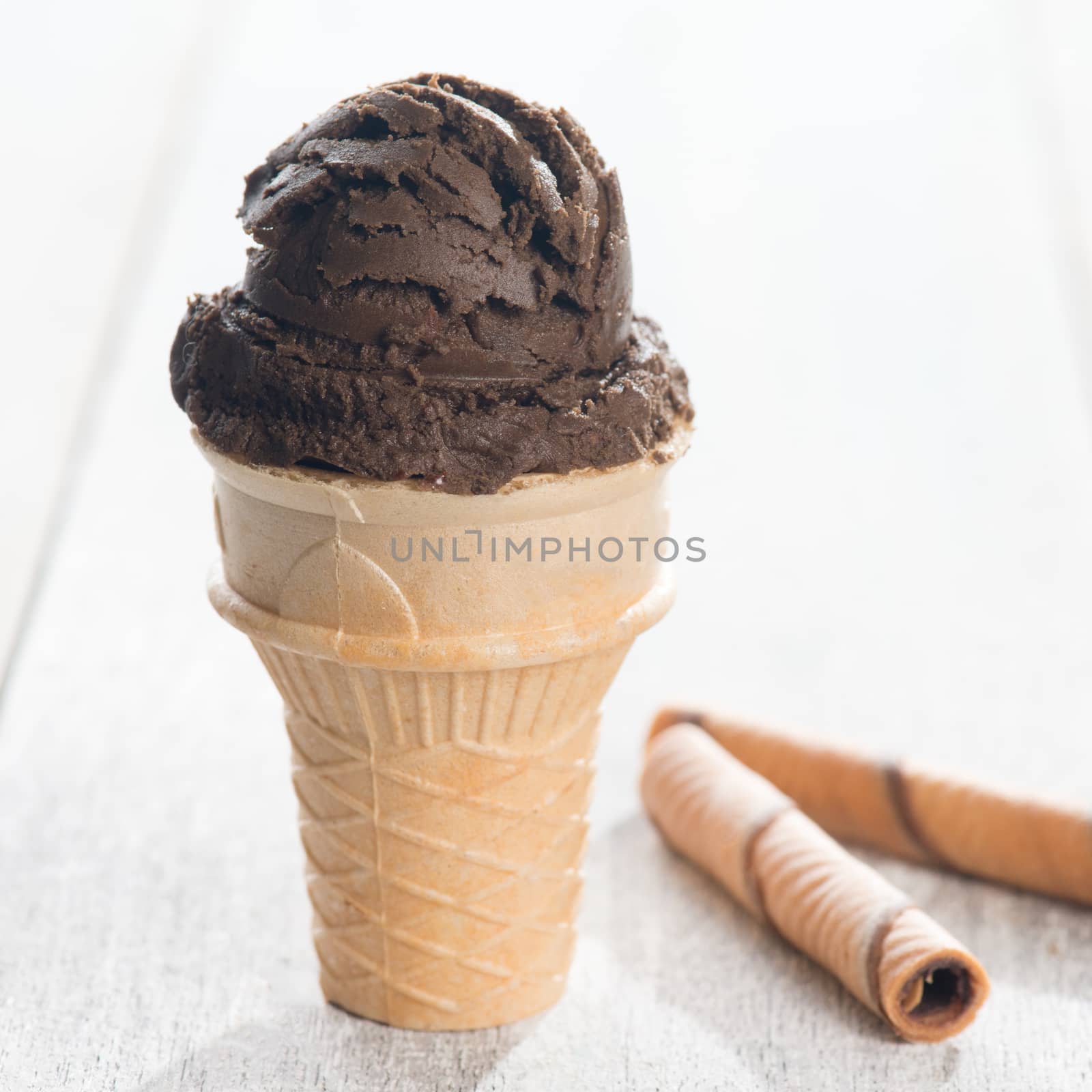 Brown ice cream in waffle cone on bright wooden background.