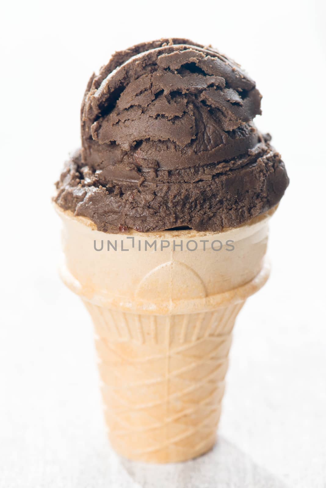 Brown ice cream in waffle cone on wooden background.