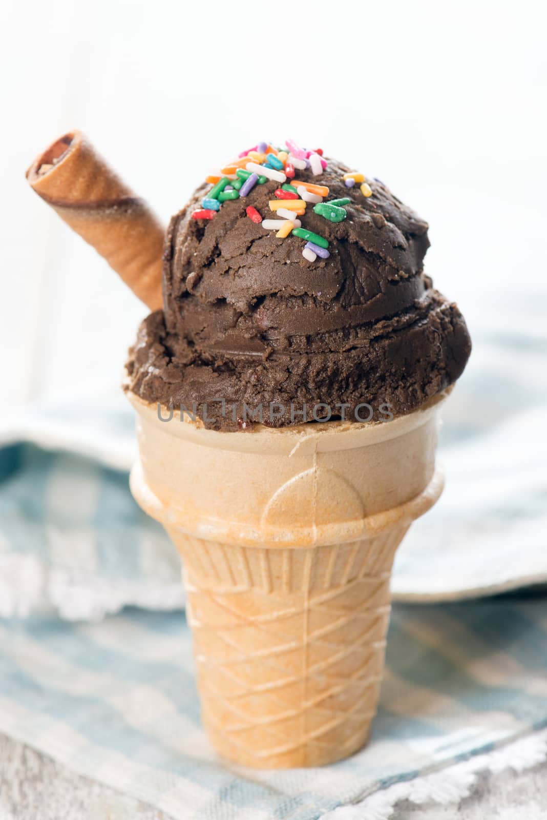 Chocolate ice cream in waffle cone on bright wooden background.