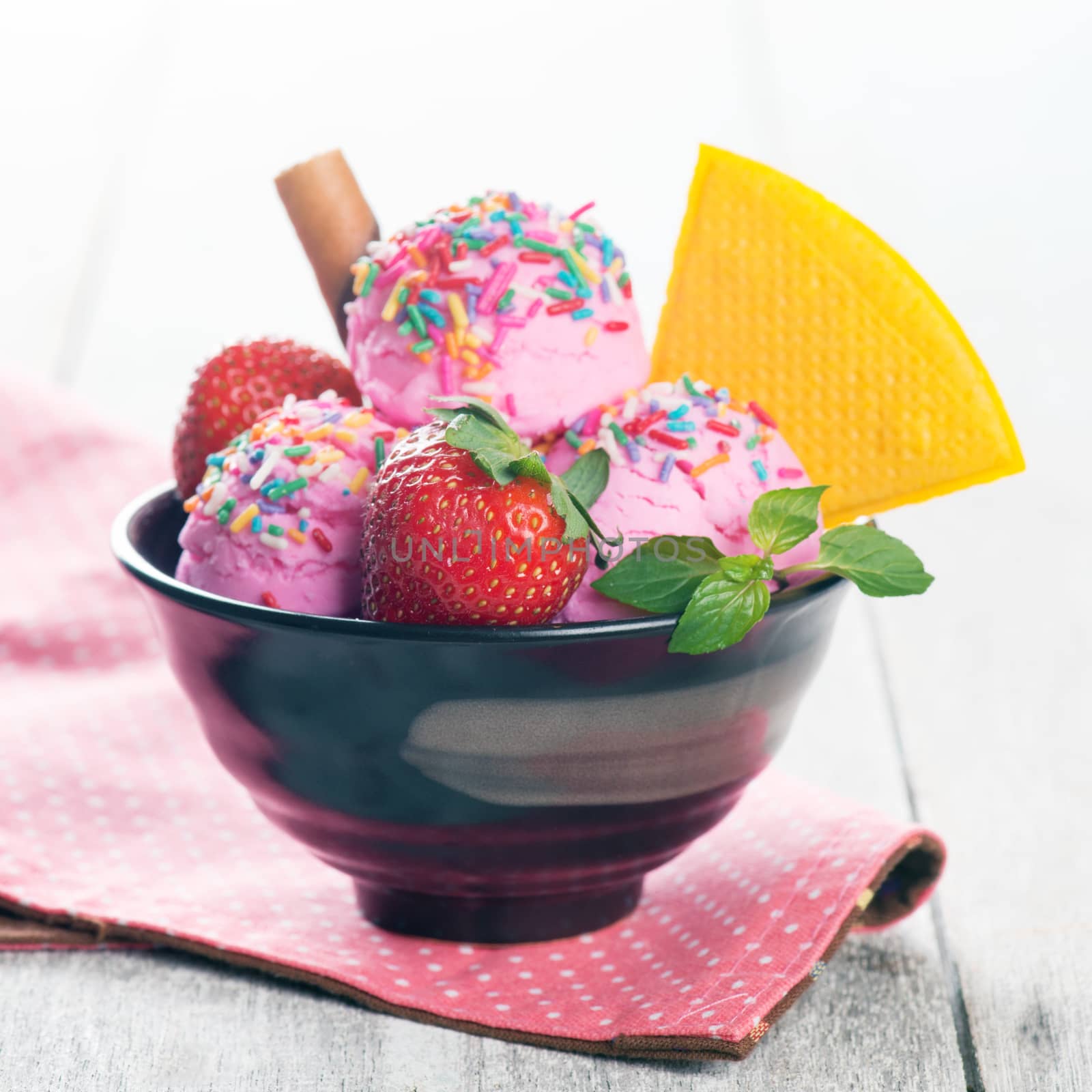Pink ice cream in bowl with strawberry fruits and waffle on white wooden background.
