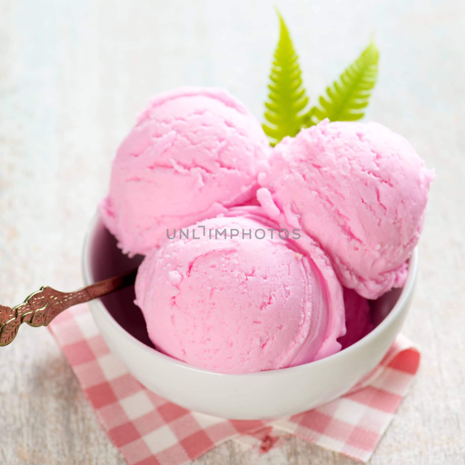 Strawberry ice cream in bowl on white wooden background.