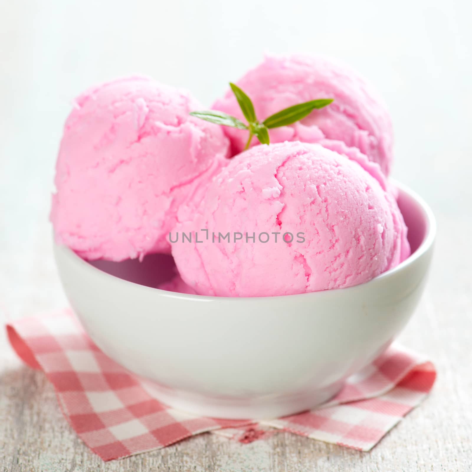 Pink ice cream in bowl on white wooden background.