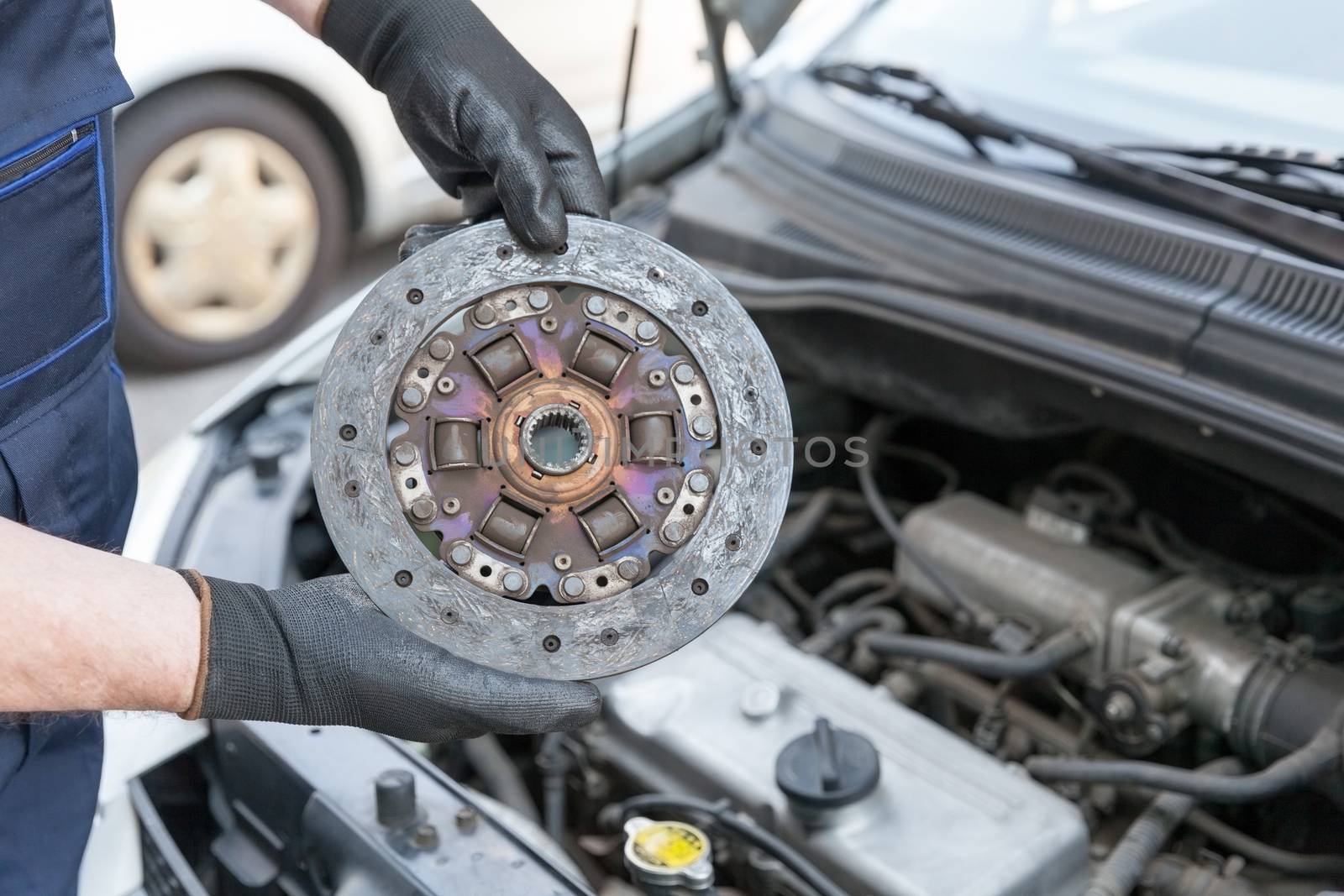 Auto mechanic wearing protective work gloves holds old clutch disc over  a car engine