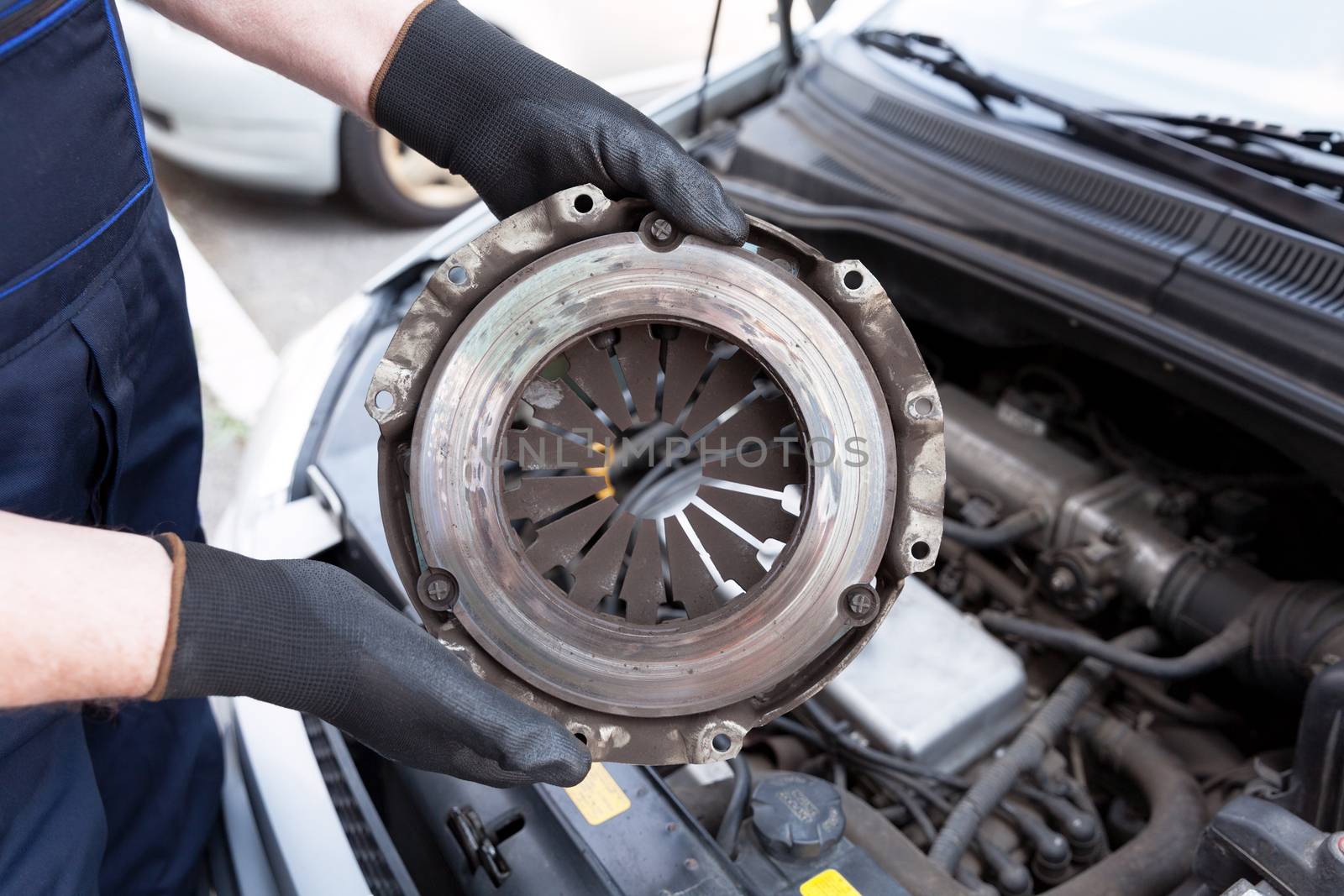 Auto mechanic wearing protective work gloves holds old clutch basket over a car engine