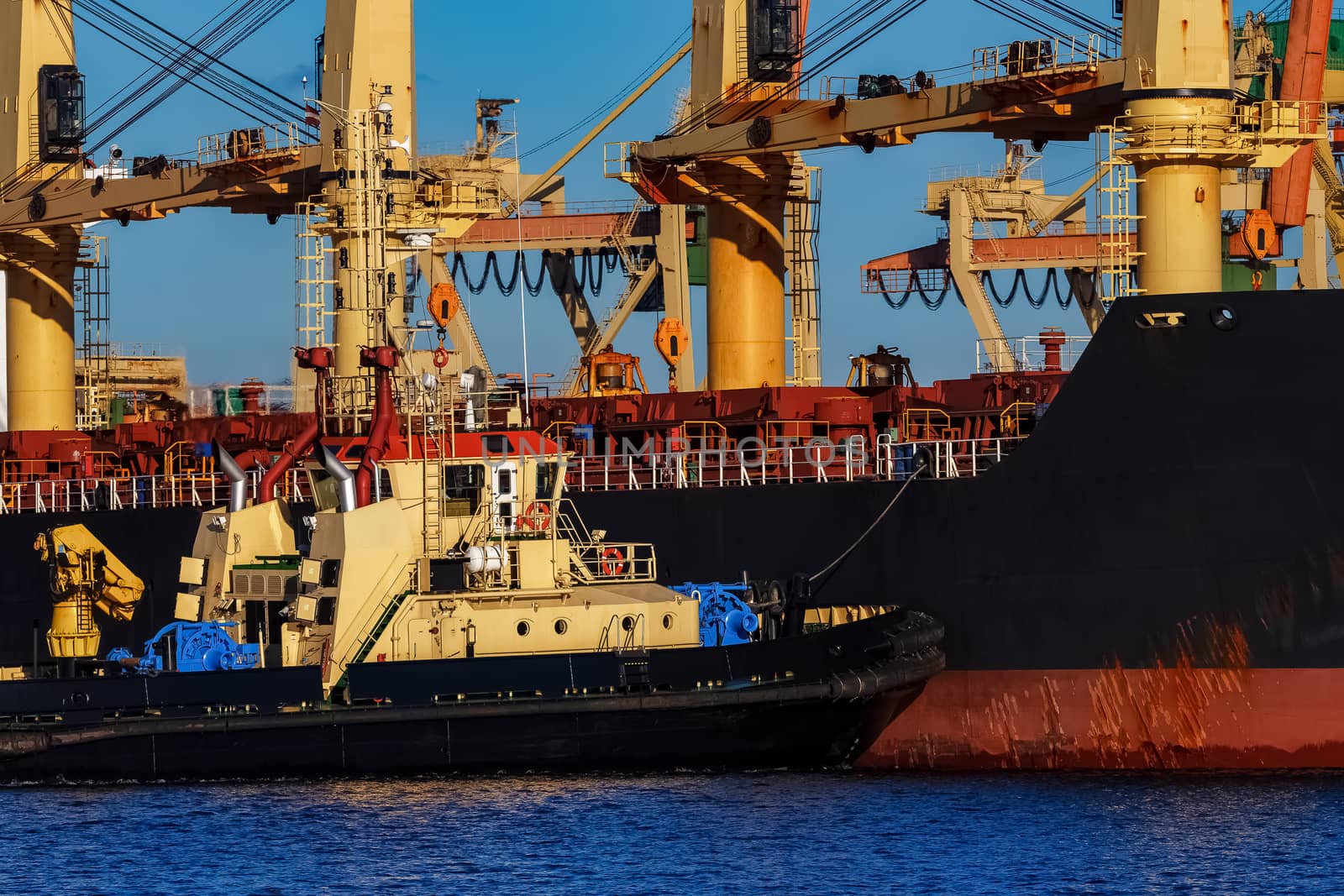 Black cargo ship mooring at the port with tug ship support