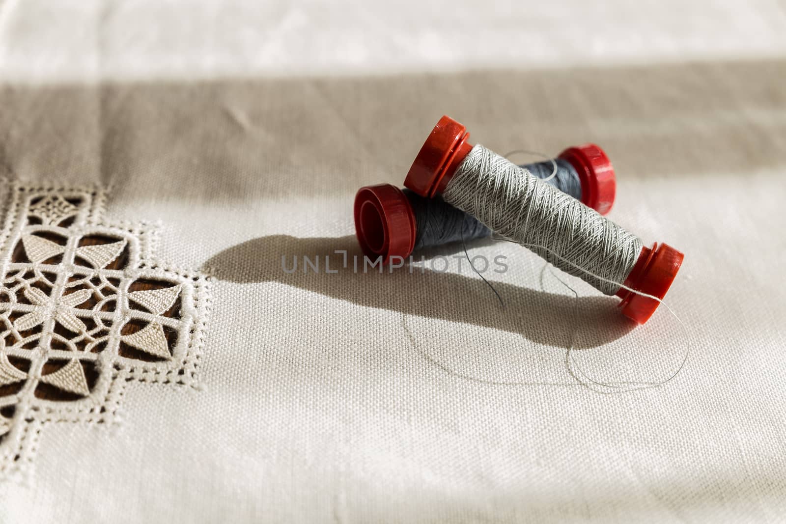 two spools of gray thread on a hand-embroidered tablecloth