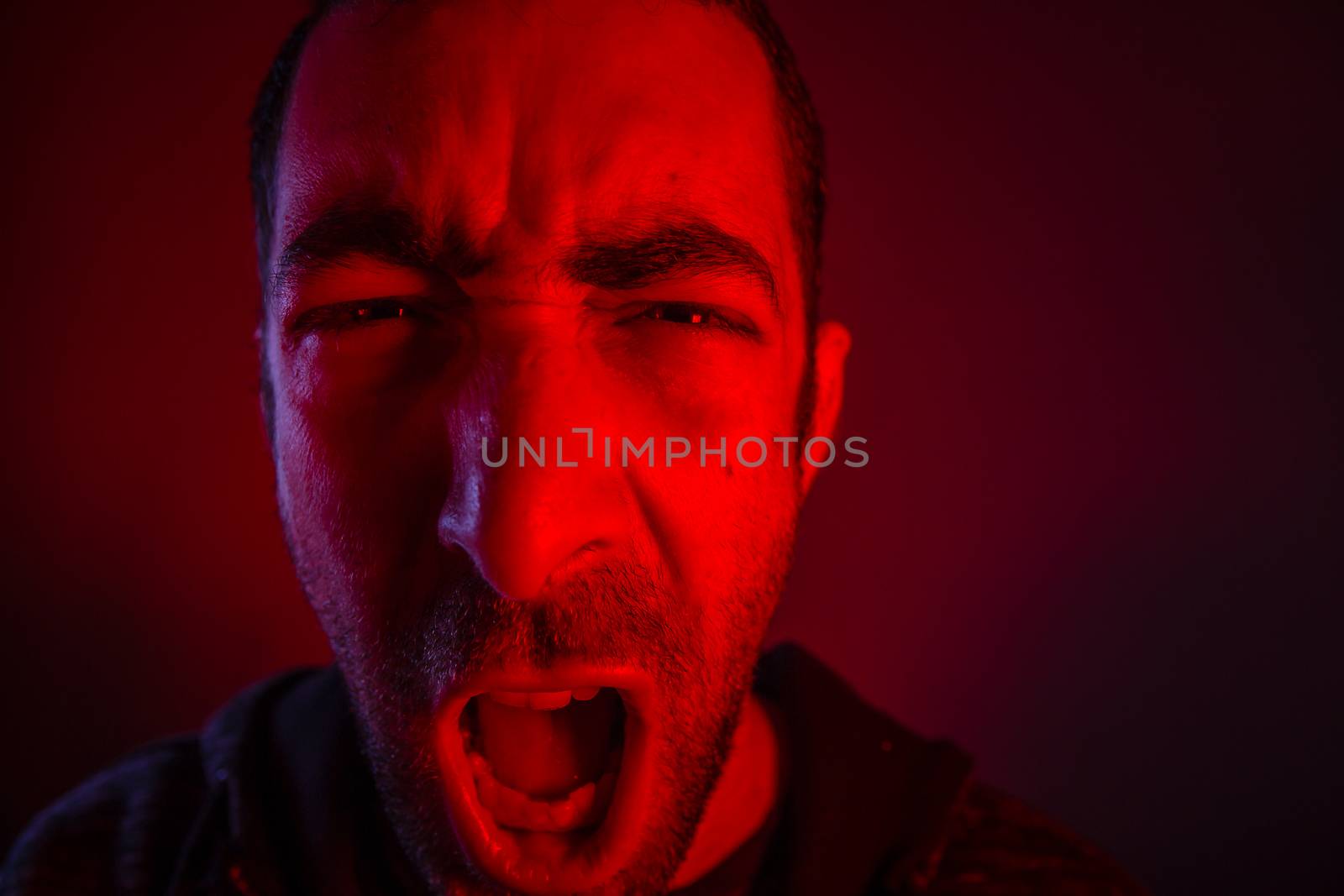 Man with angry facial expression screaming out loud. Close up portrait of a man shouting with mouth wide open.