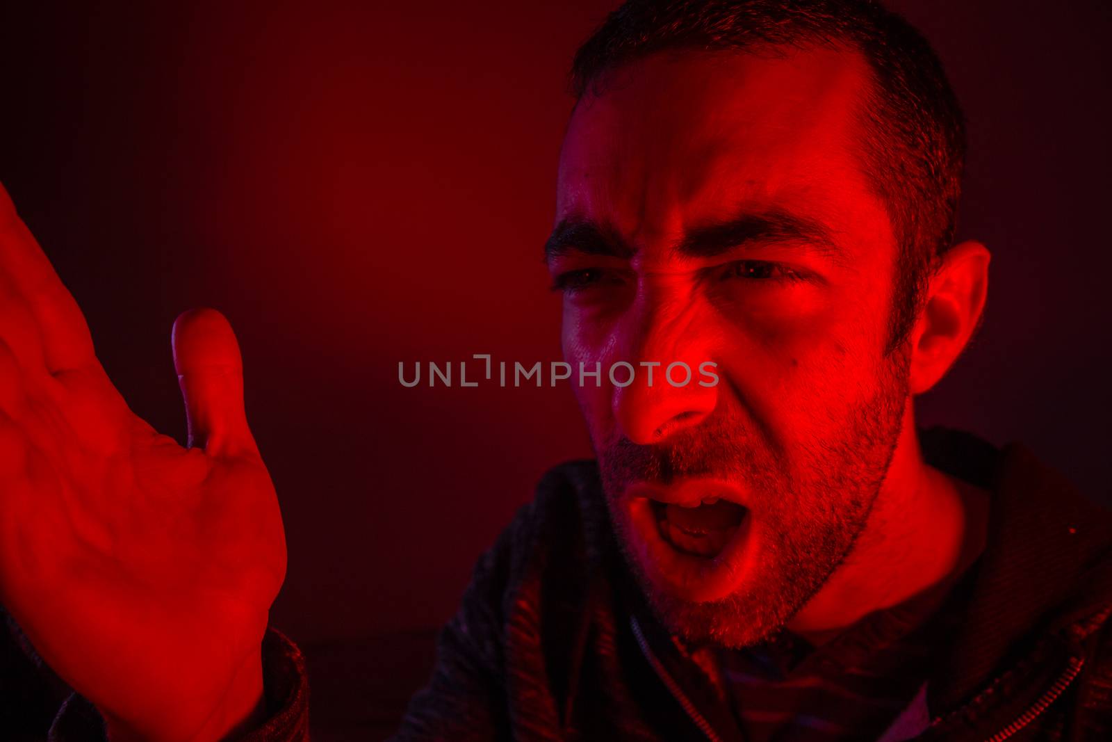Man with angry facial expression screaming out loud and waving with his hand. Close up portrait of a man shouting with mouth wide open.