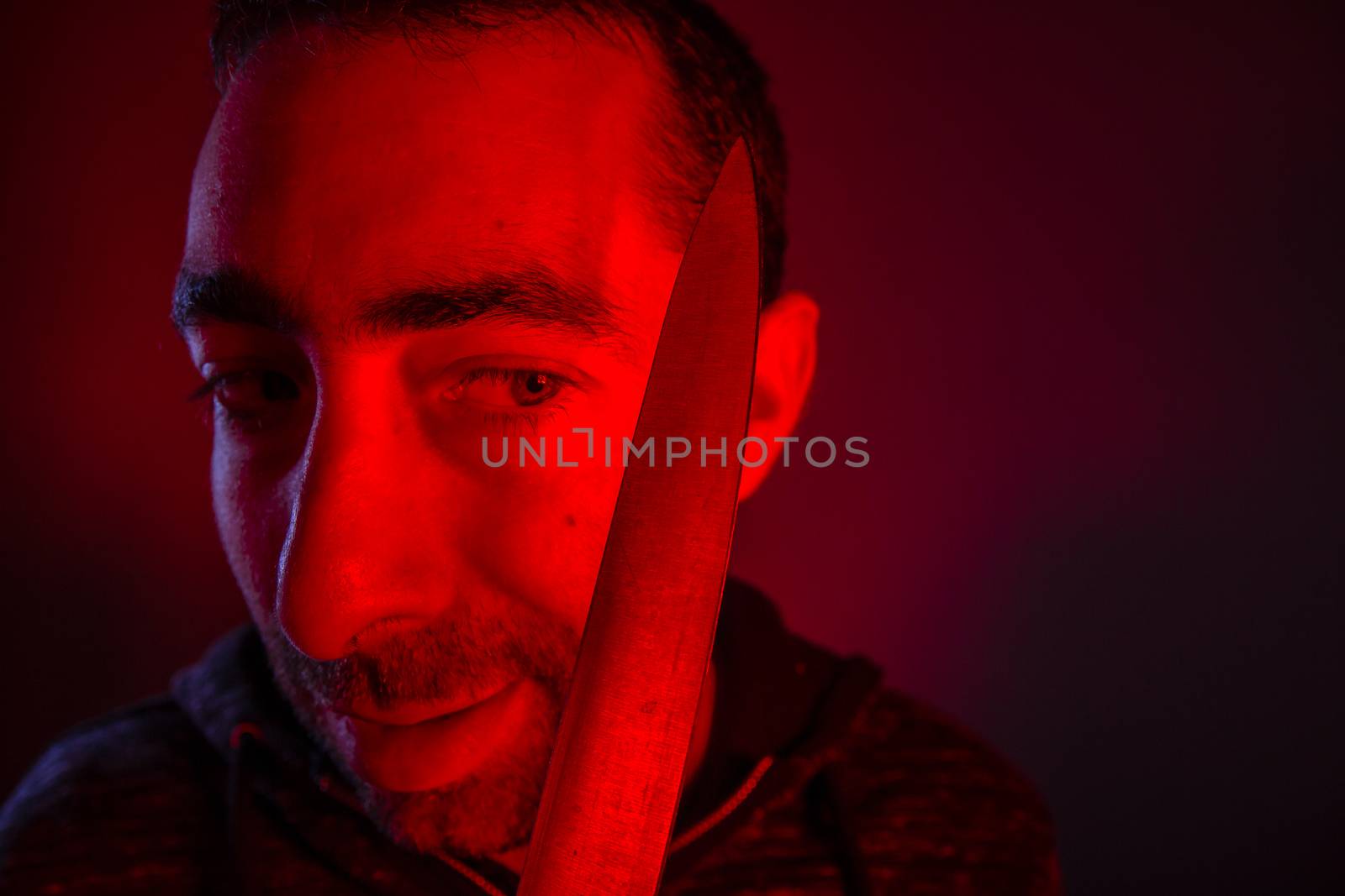 Closeup of sinister man looking at a knife that he holding.