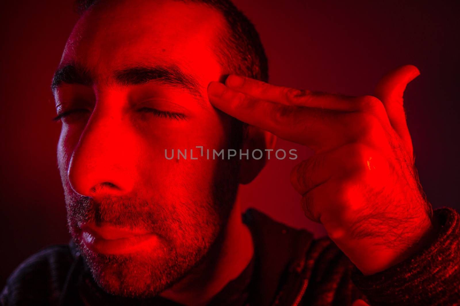 Closeup of sad young man committing suicide with finger gun gesture.