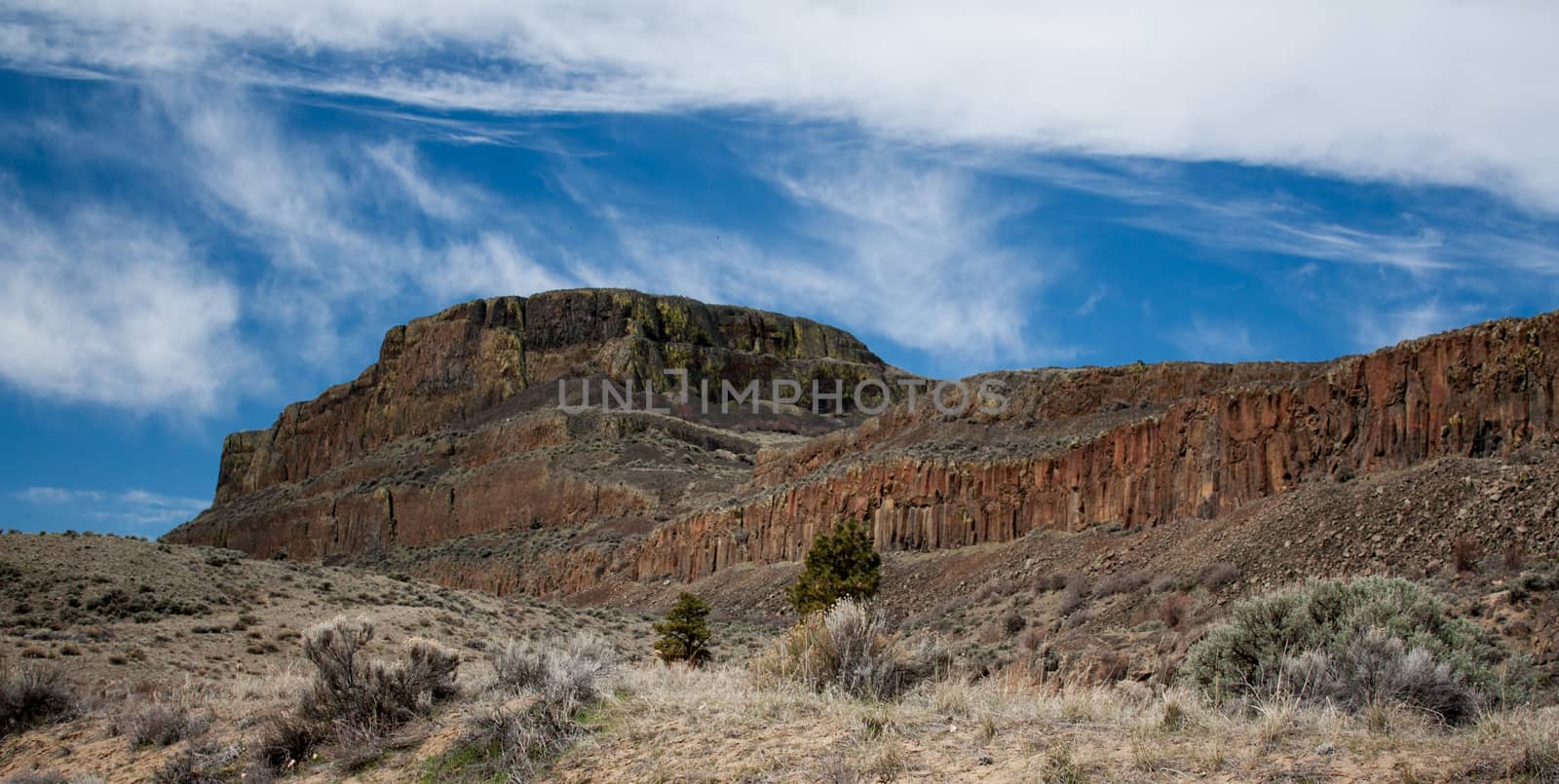 Red desert peak with a blue sky and scrub brush by experiencesnw