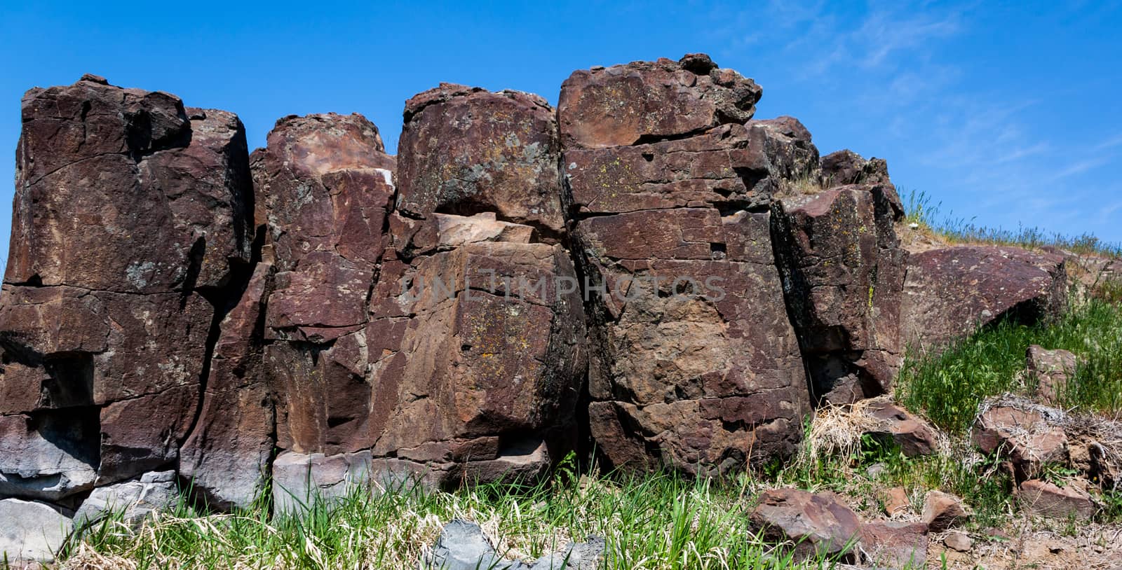 Red desert rocky hillside with rough cracked stones and grass