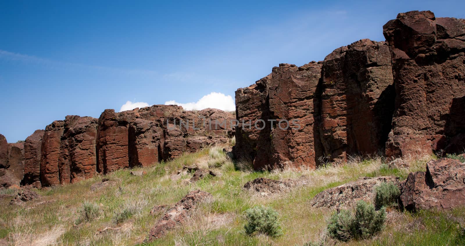 Red rocky desert cliffs under a blue sky with grass