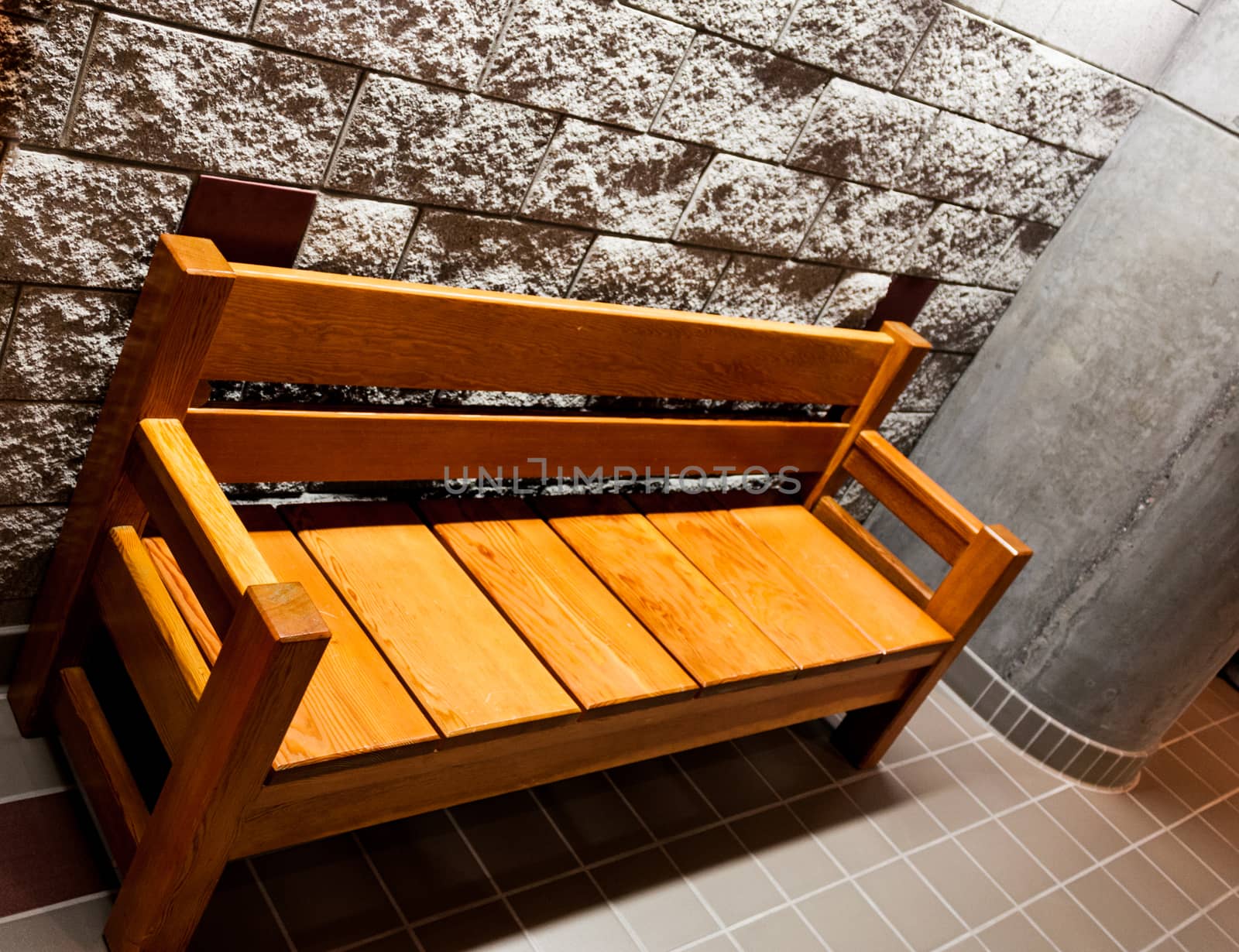 Sturdy wooden bench in front of a rough white stone wall next to a pillar