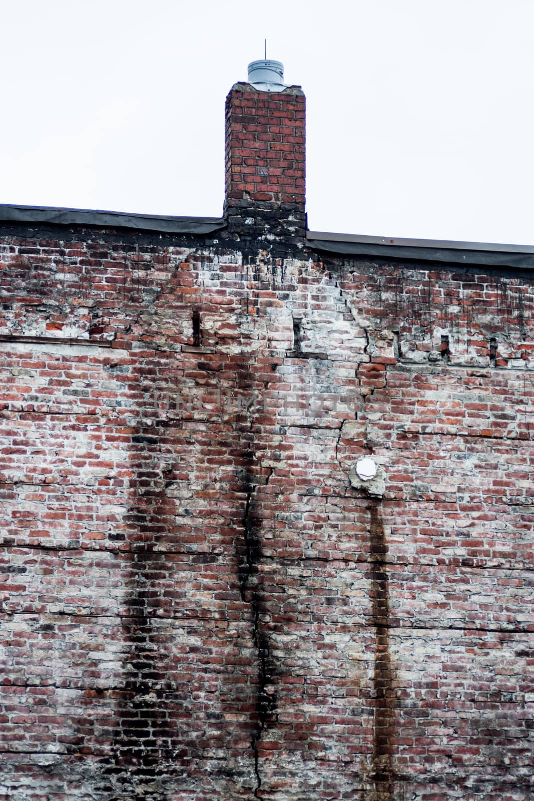 Old eroded stained brick wall with chimney