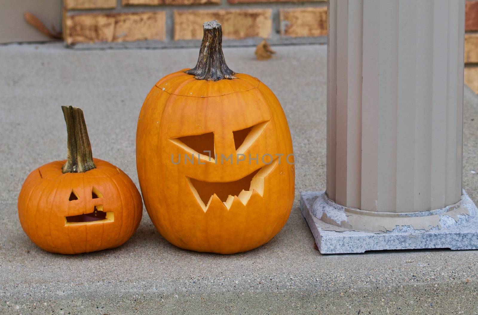 Two jack o lanterns site beside a pillar.