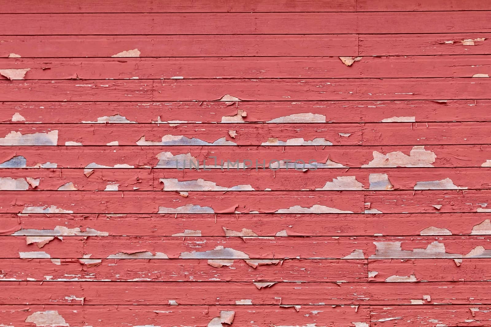 Horizontal rows of barn siding show with peeling red paint.