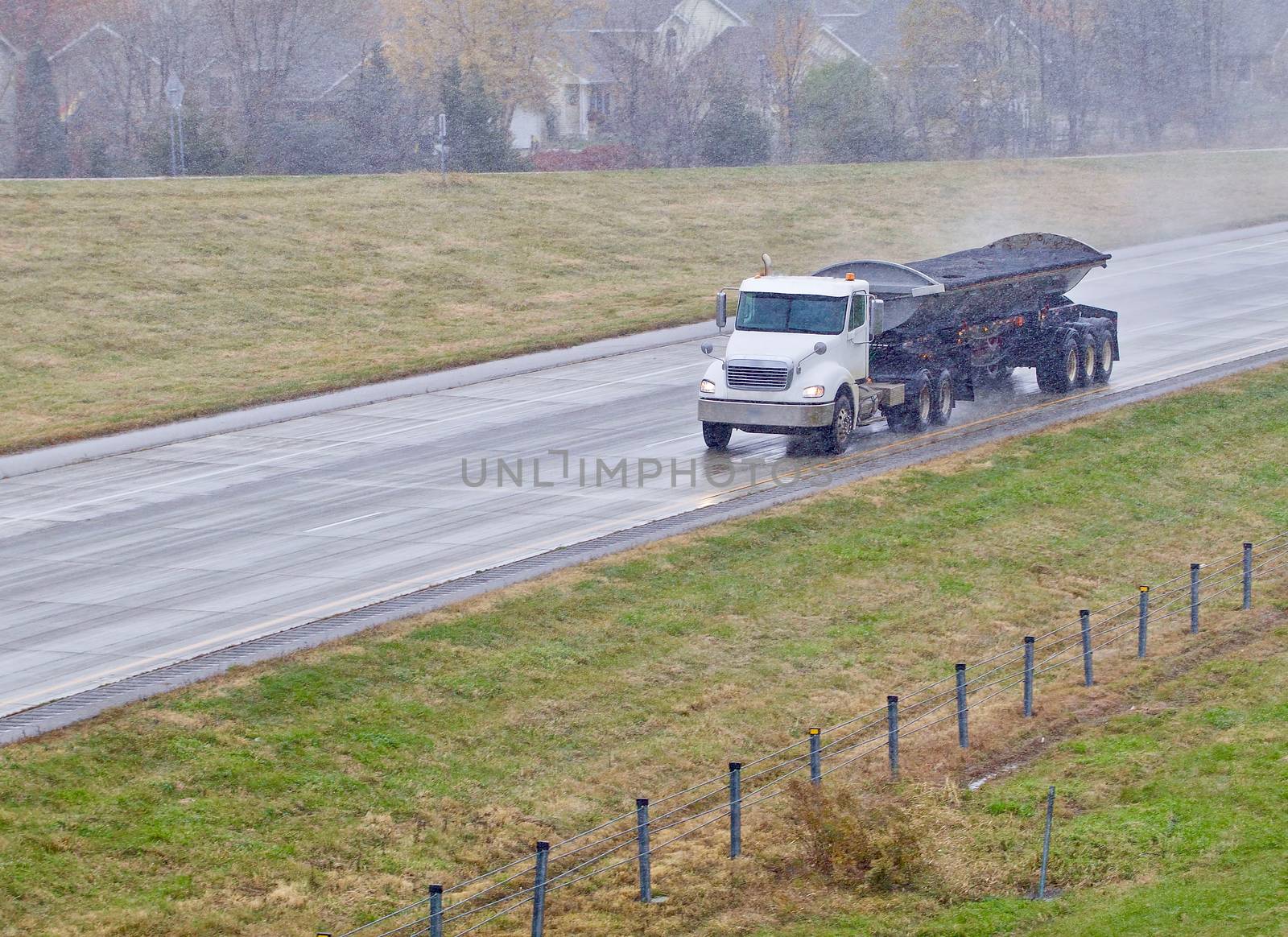 A wet dump truck hauling black dirt speeds down a wet highway in the pouring rain.