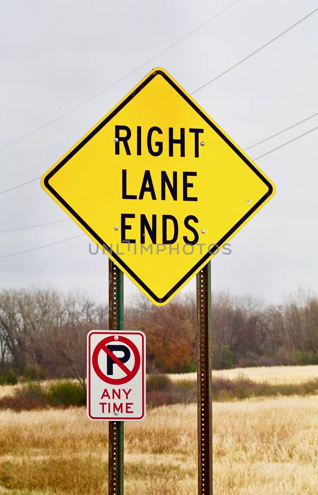 A bright yellow right lane ends warning sign shows against a rural background.