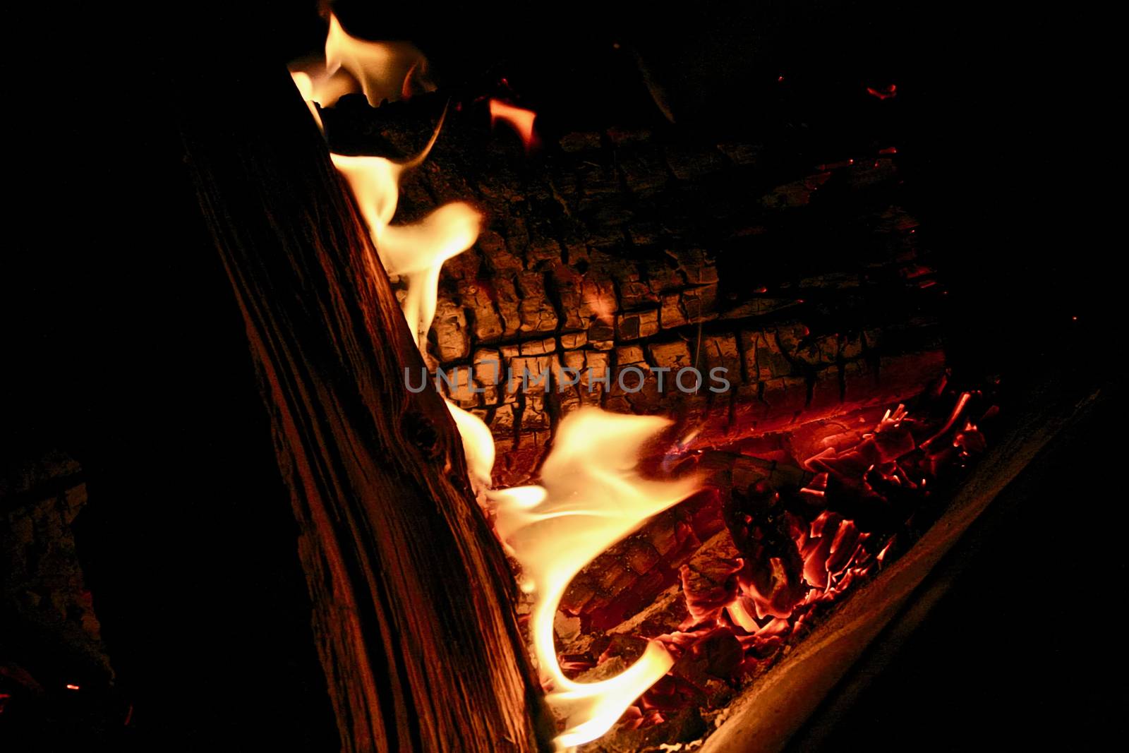 Dancing flames appear on the charred wood amidst the glowing coals.