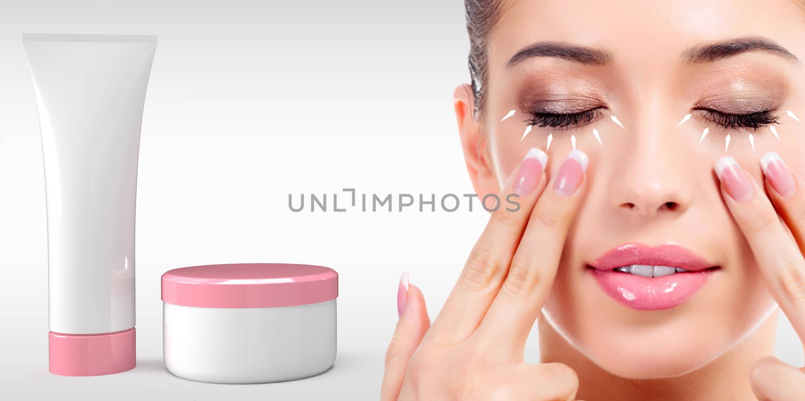 Woman massaging her face with fingers and cosmetics tube and jar on light grey background