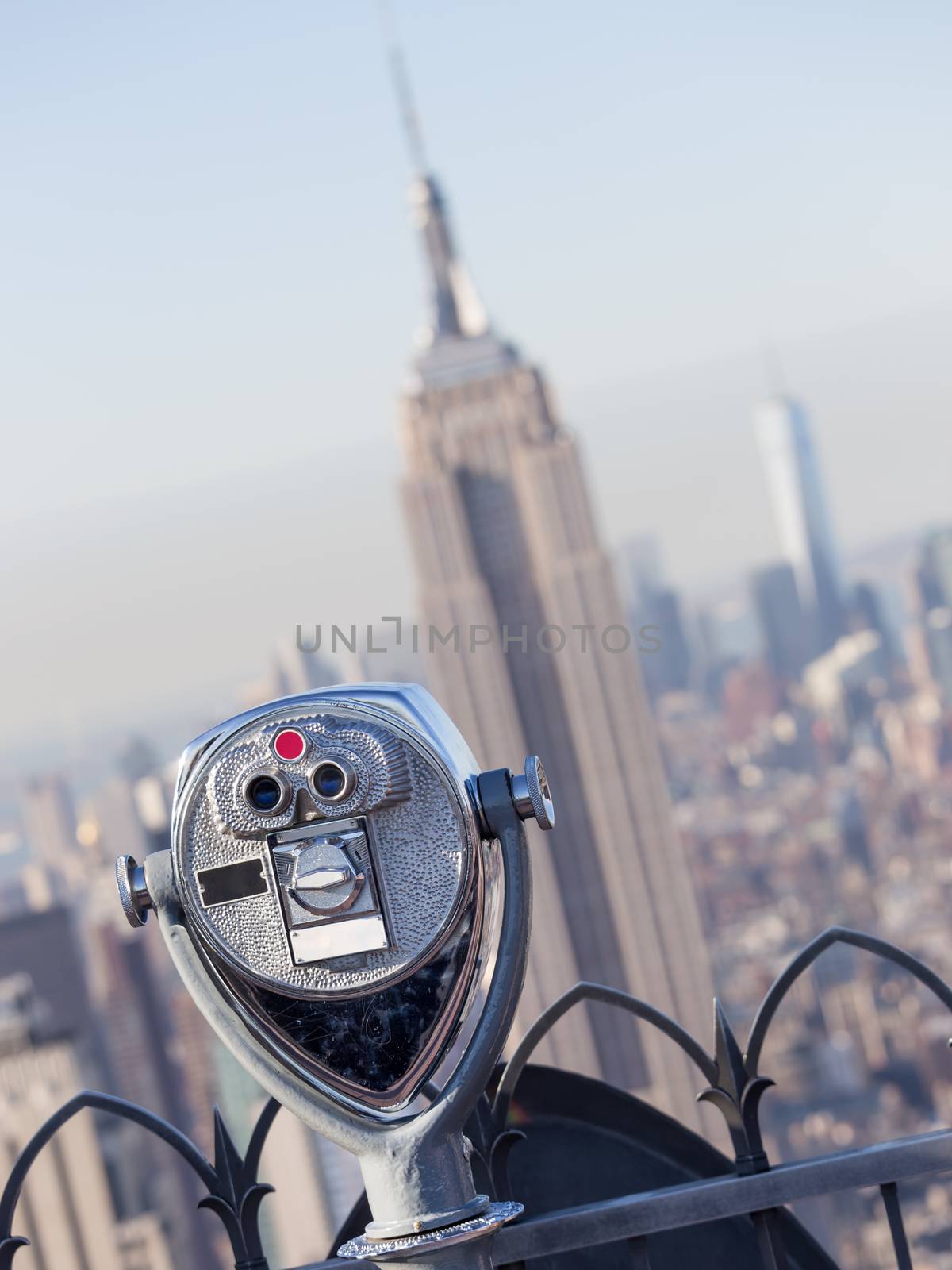 New York City, USA. Vintage tourist binoculars at Top of the Rock observation deck in front of Manhattan downtown skyline with Empire State Building and skyscrapers at sunset.
